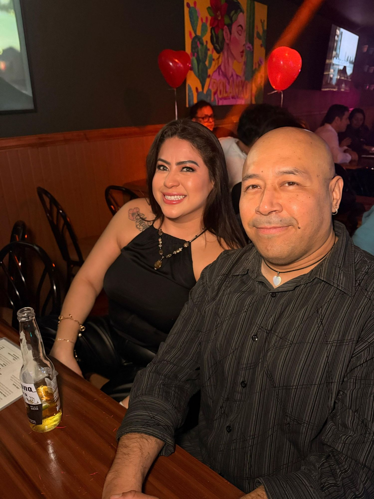 Two people sitting at restaurant table with red balloons in background.