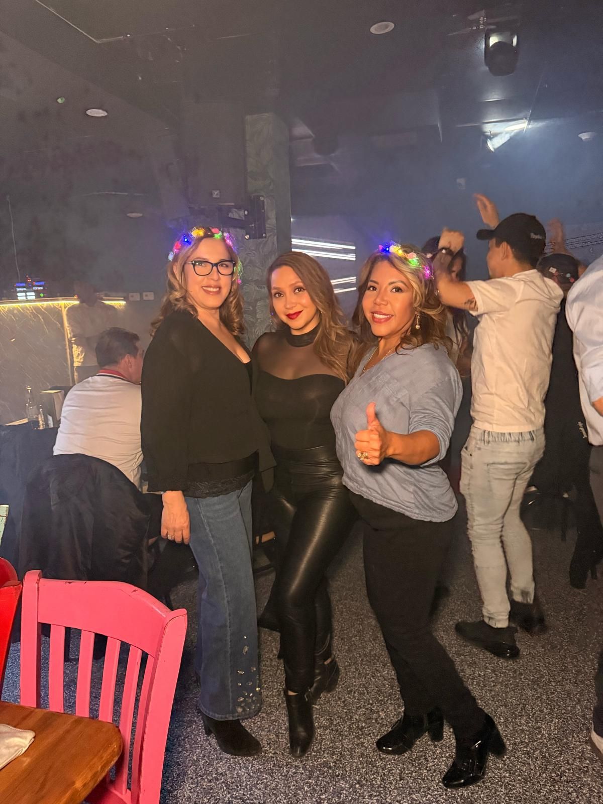 A group of people dancing and socializing in a dimly lit venue with a pink chair visible in the foreground.