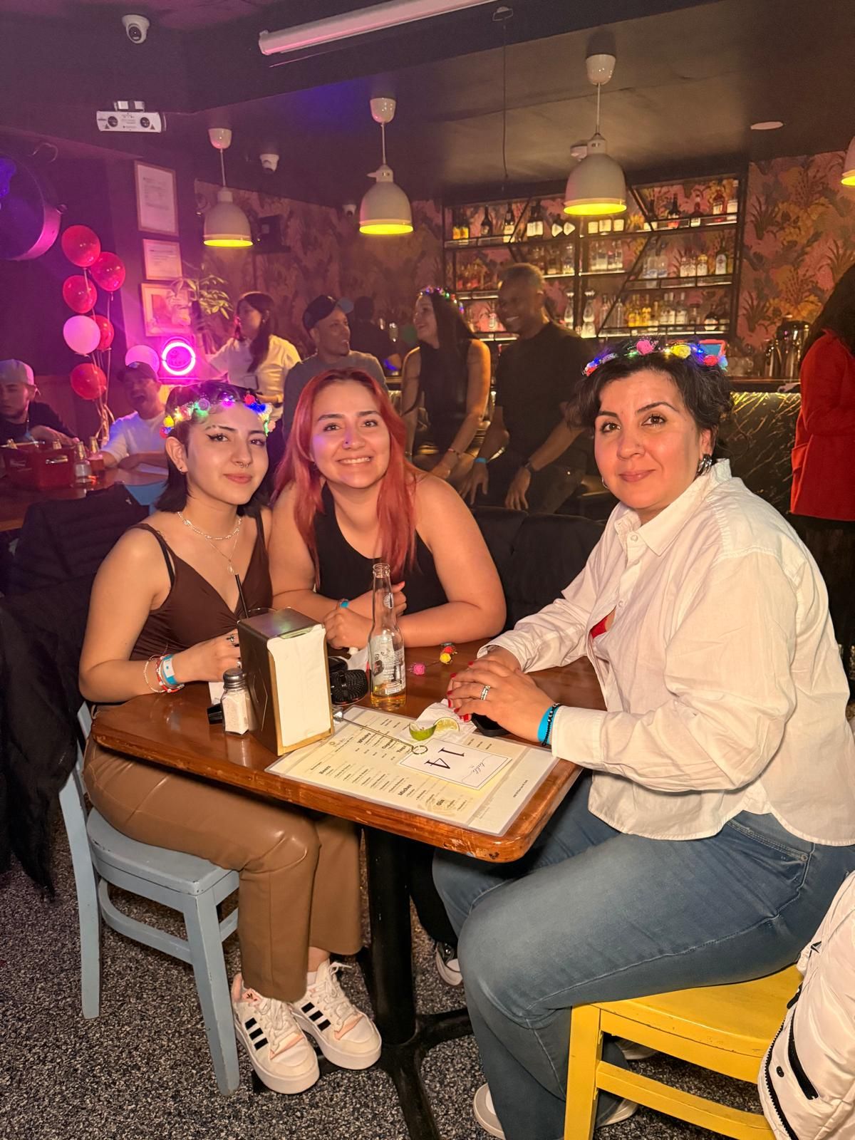 People gathered around a table in a dimly lit bar with purple and pink lighting creating a festive atmosphere.