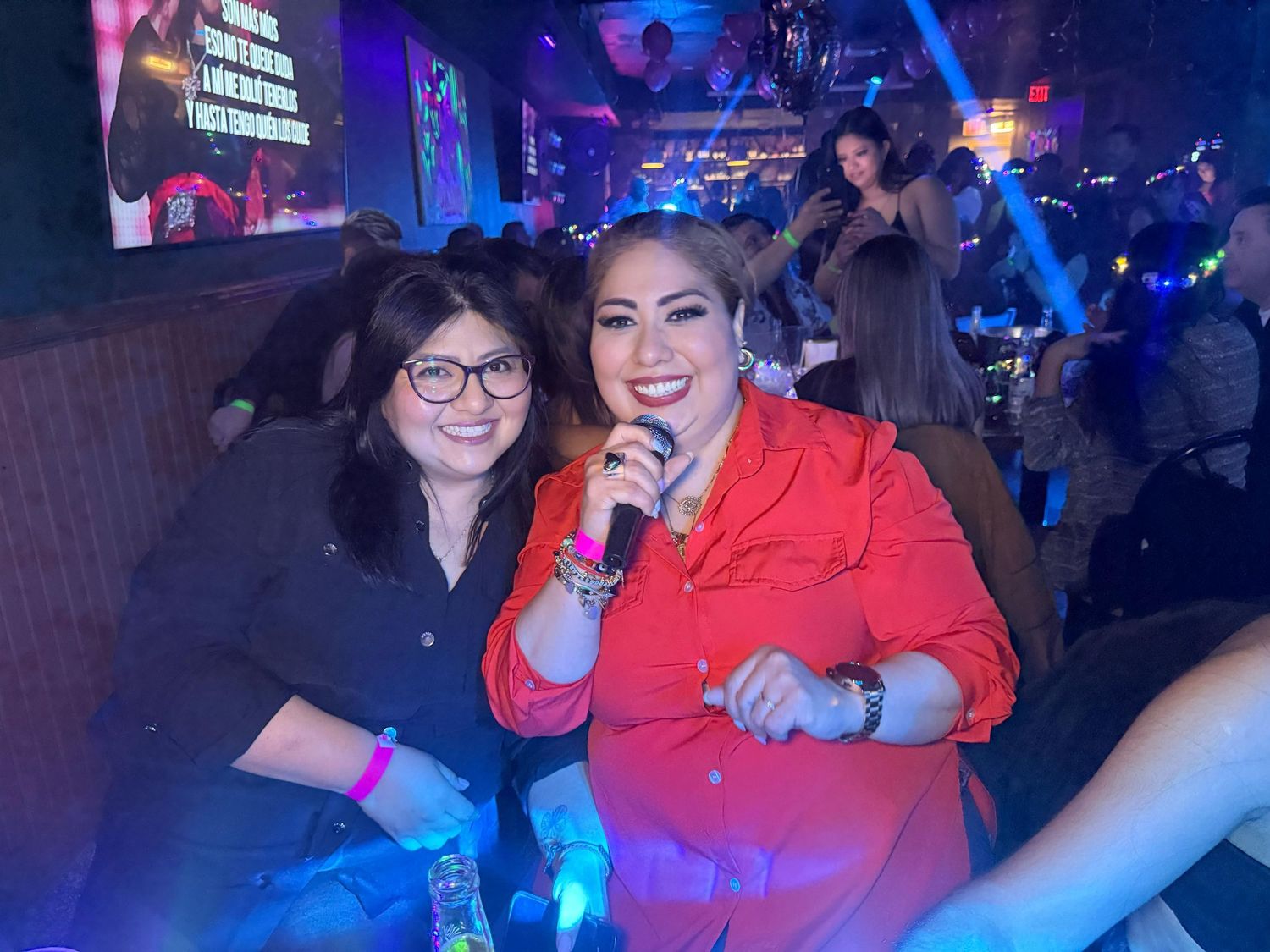 Group celebrating with drinks under colorful party lights.
