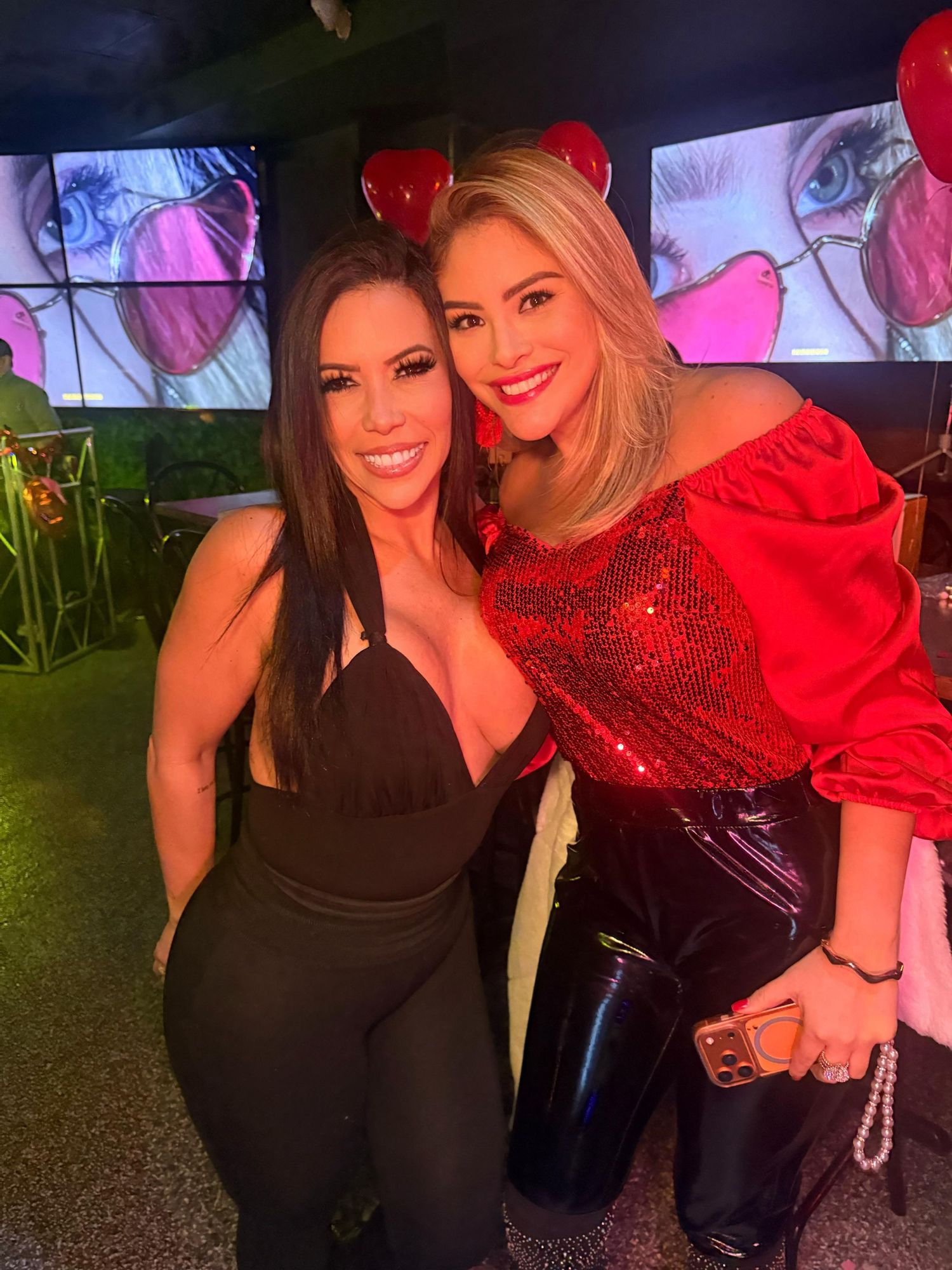 Two friends pose together at a nighttime event wearing black and sparkly red outfits.