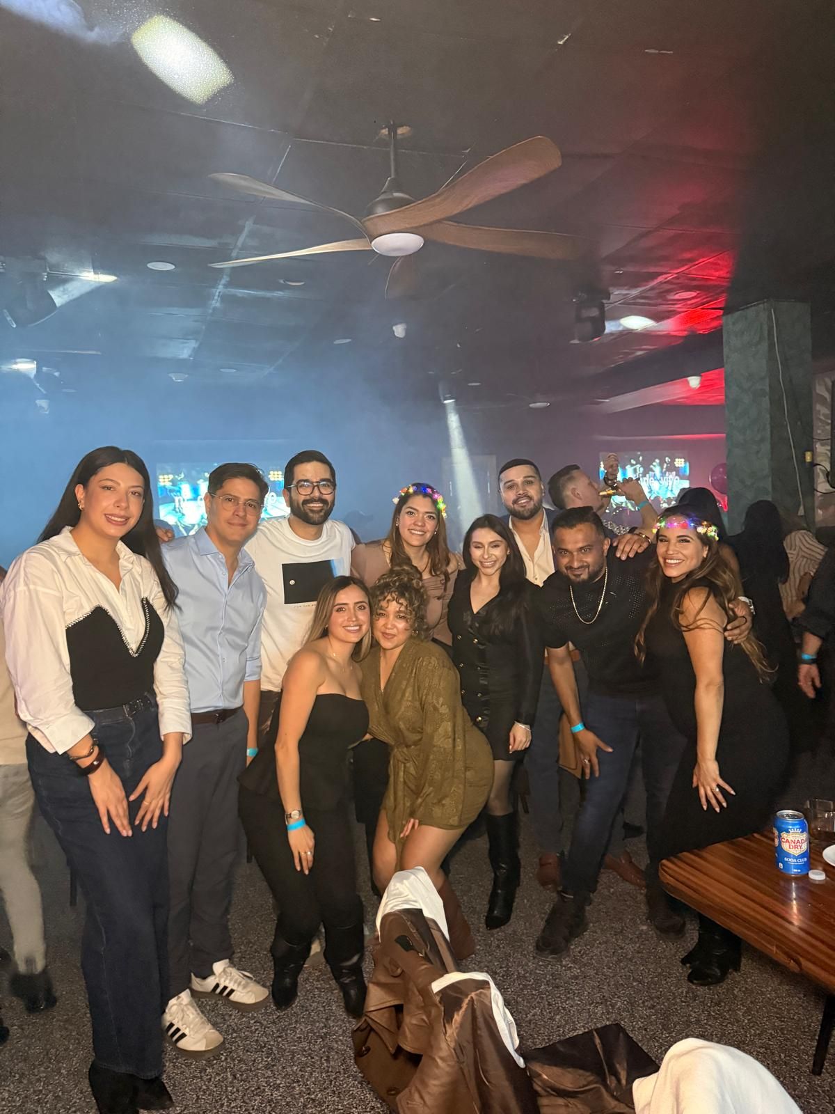 A group of people posing together at what appears to be a party or social gathering with dim lighting and atmospheric effects.