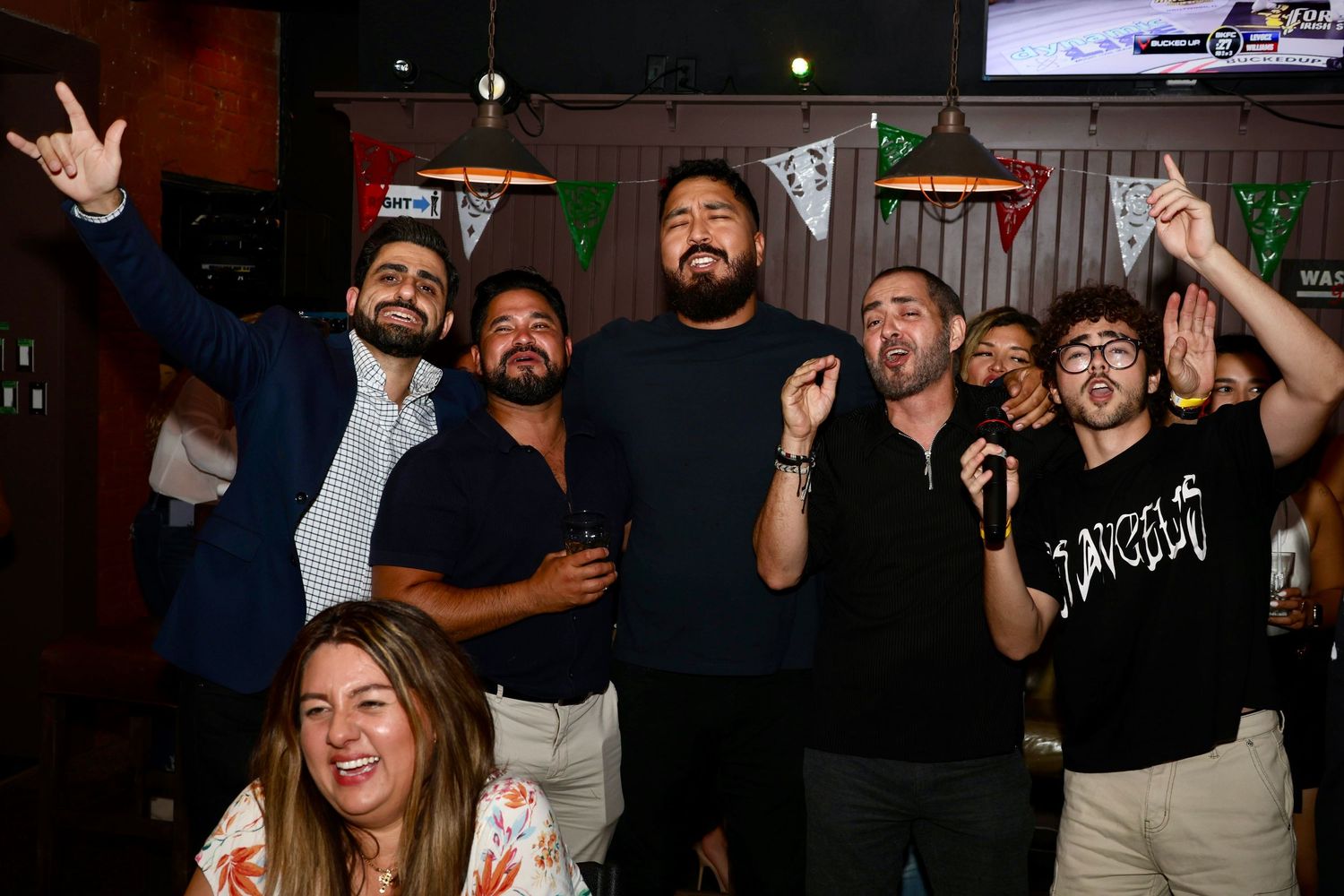 Group of people celebrating at a nightclub with raised hands and excited expressions.