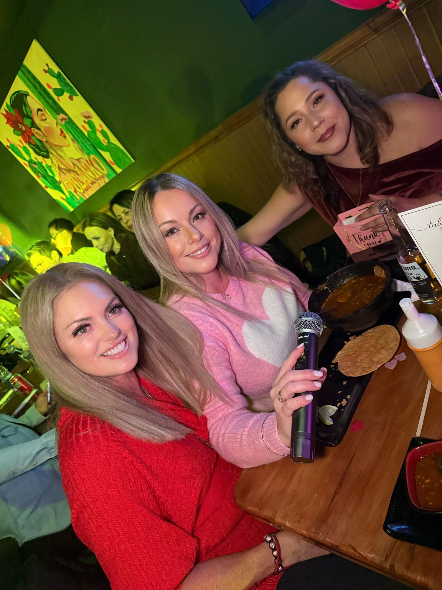 Three friends at a restaurant table with microphone and food.