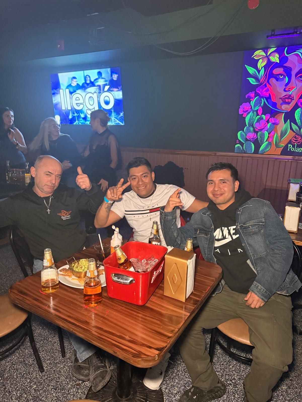 Group of friends enjoying drinks and food at a dimly lit bar with neon lighting and wooden tables.