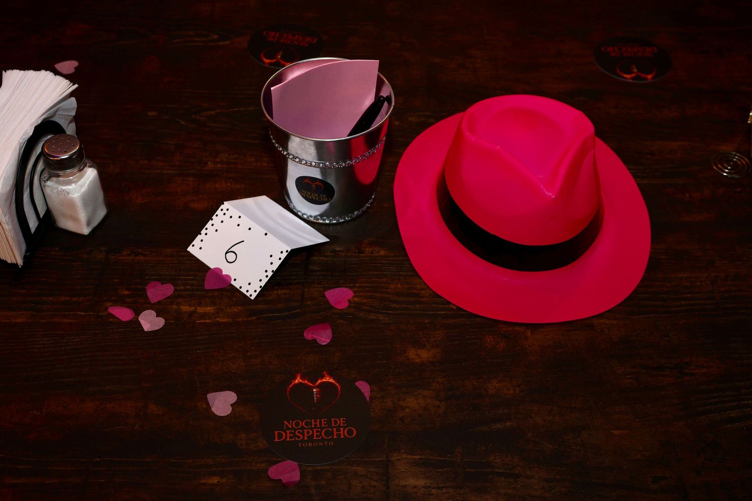 Red hat and pink heart decorations arranged on dark wooden surface.