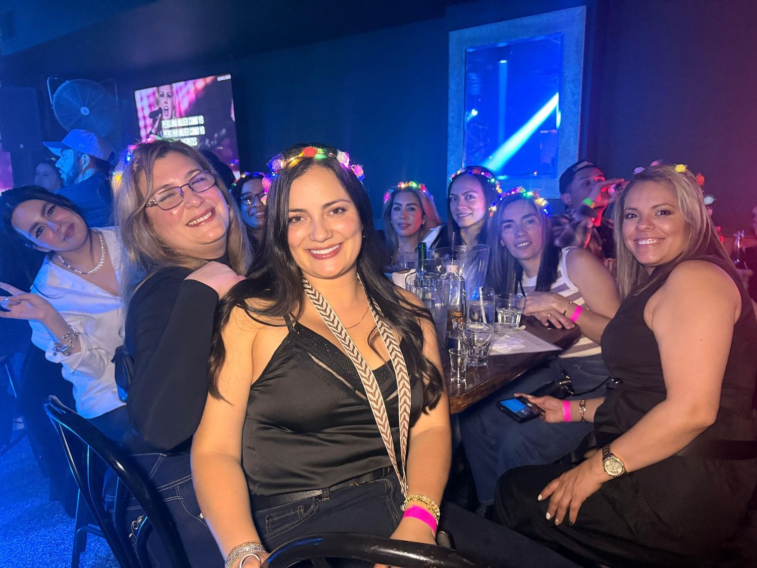 A group enjoys a night out at a dimly lit bar with blue lighting and drinks on the table.