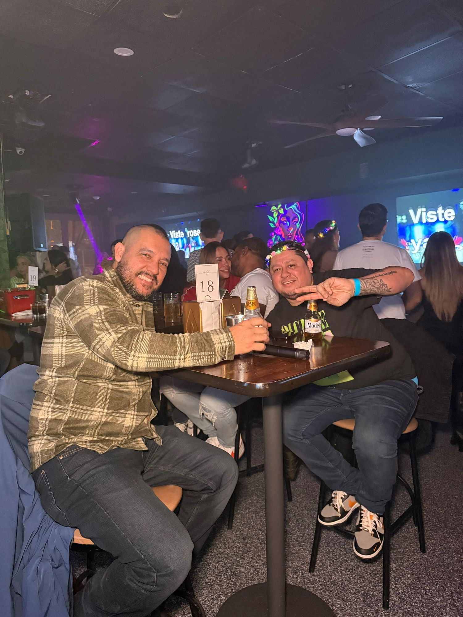 Three friends share drinks at a bar table with purple ambient lighting in the background.