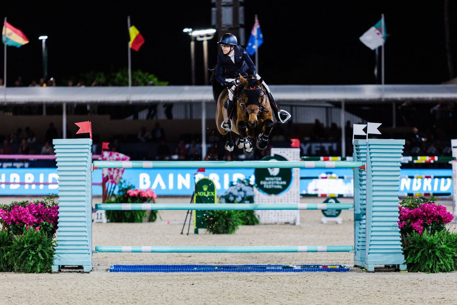 Horse and rider clearing a show jumping fence on an outdoor course with decorative blue and white standards.
