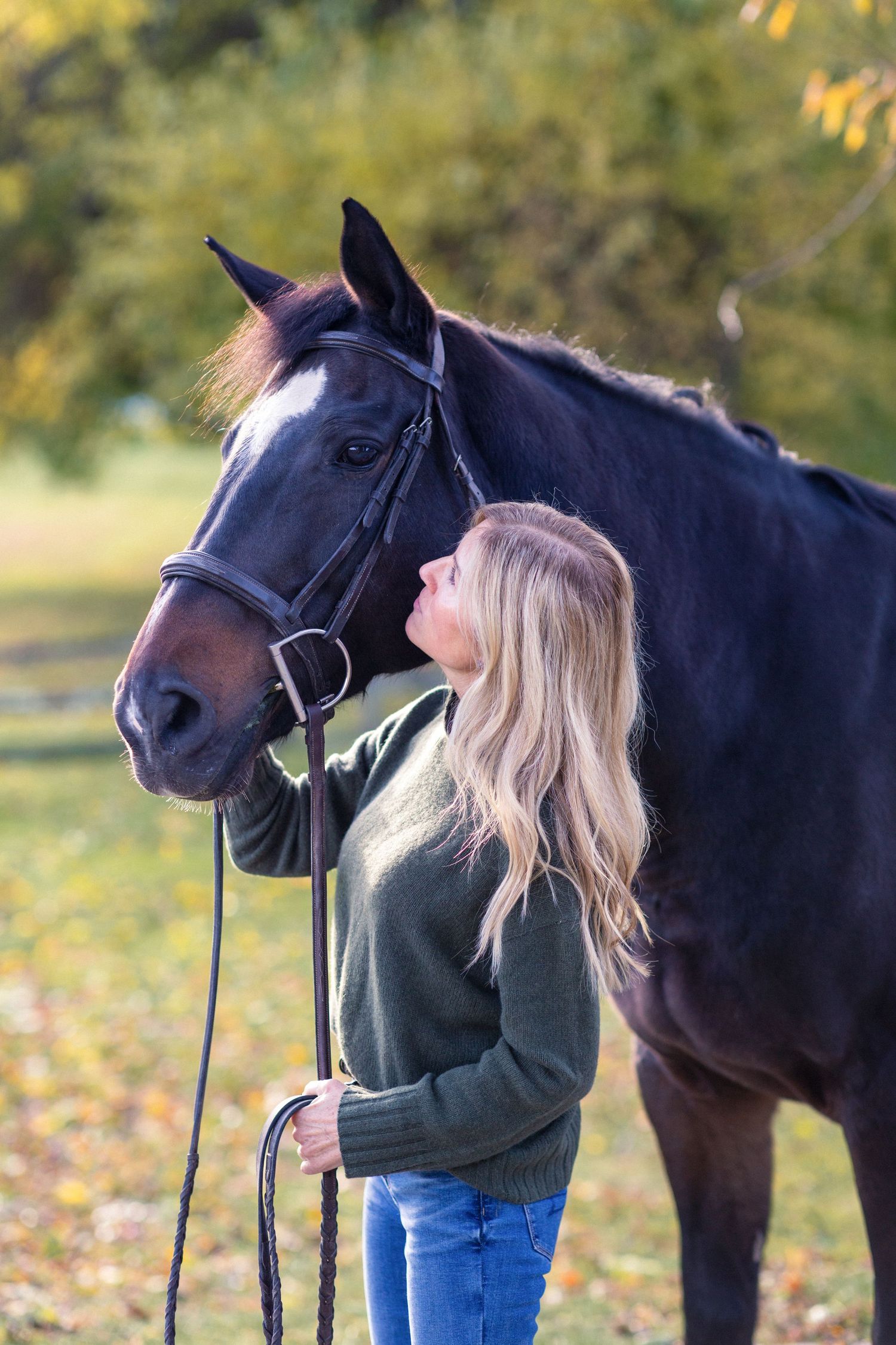 A dark brown horse and rider share an intimate moment against a fall backdrop with autumn leaves.