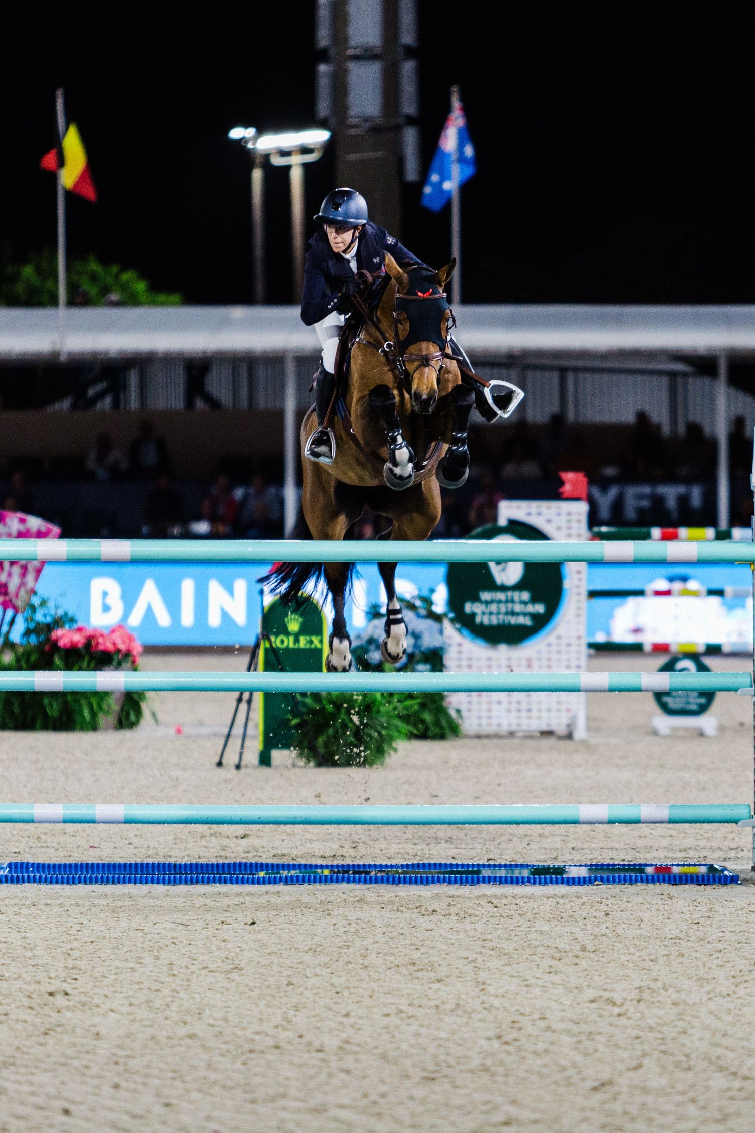 Professional equestrian jumping sequence showing horse and rider clearing obstacles in sandy arena during competition.