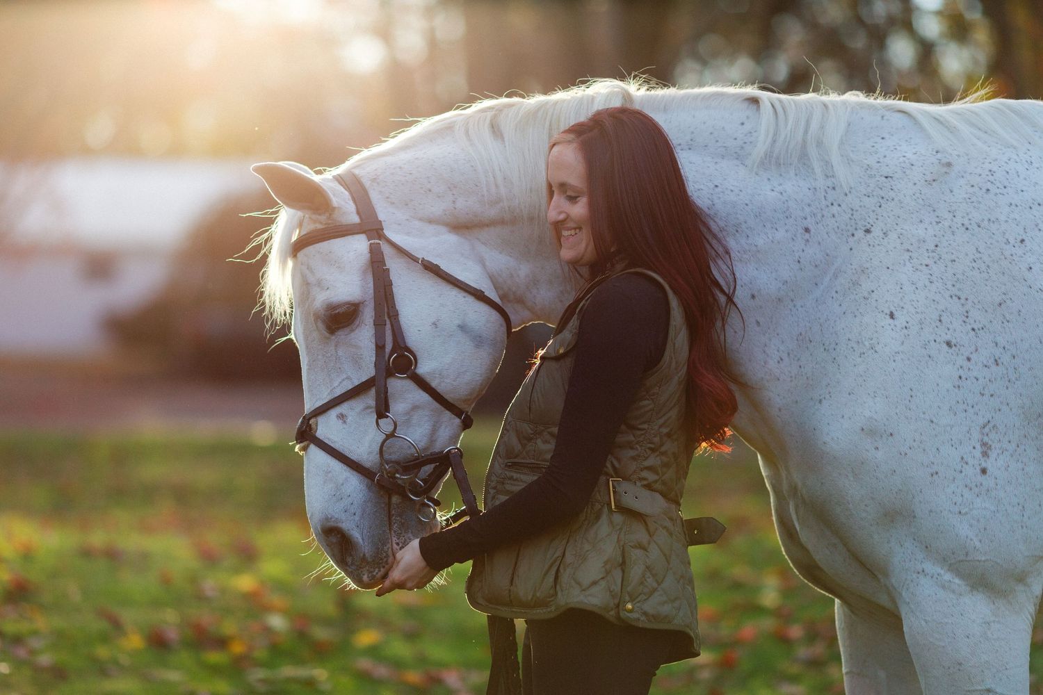 A white horse and rider share a tender moment in golden sunlight during sunset.