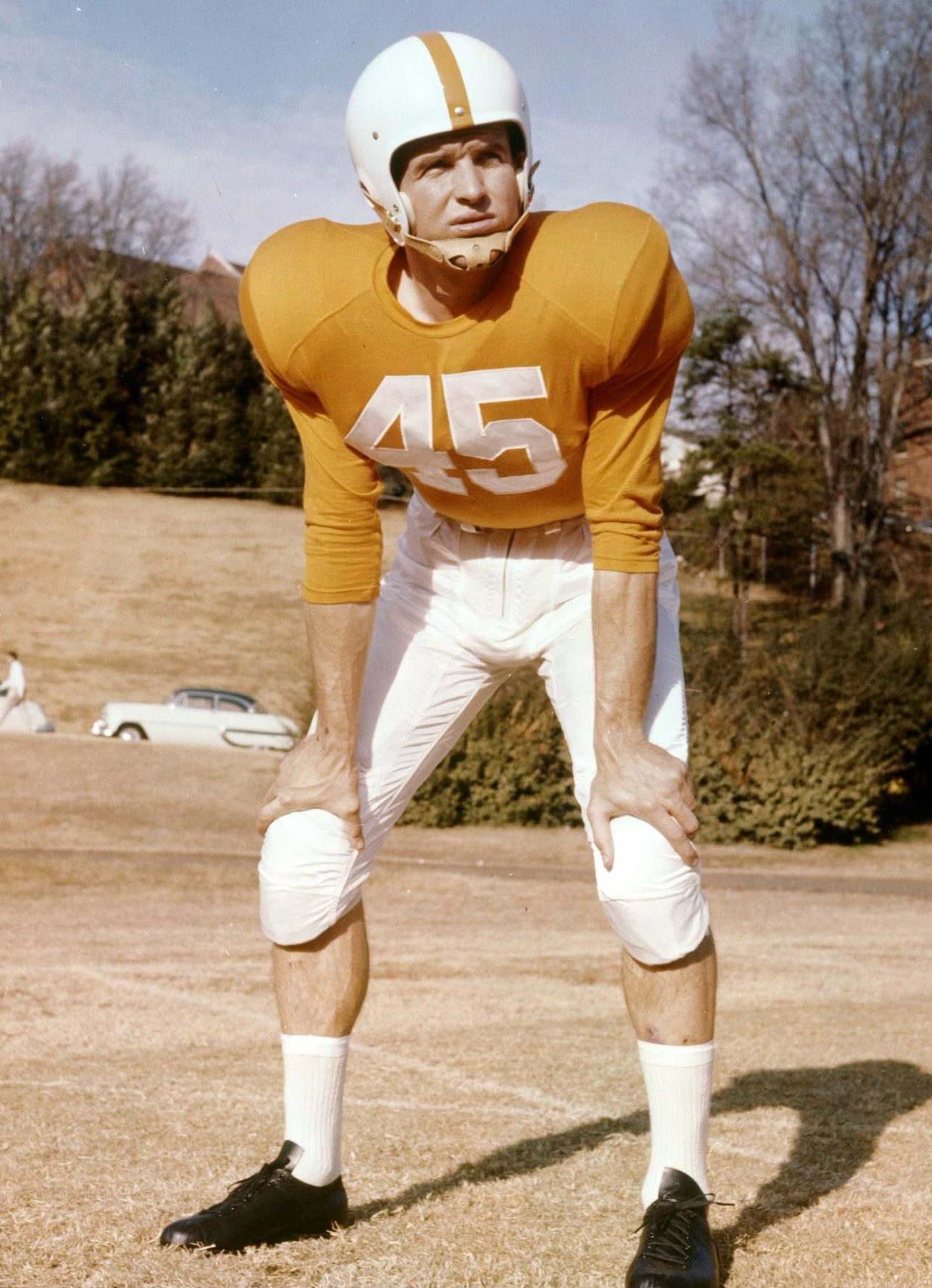 Vintage football player in yellow jersey and white pants demonstrates various athletic stances on practice field.
