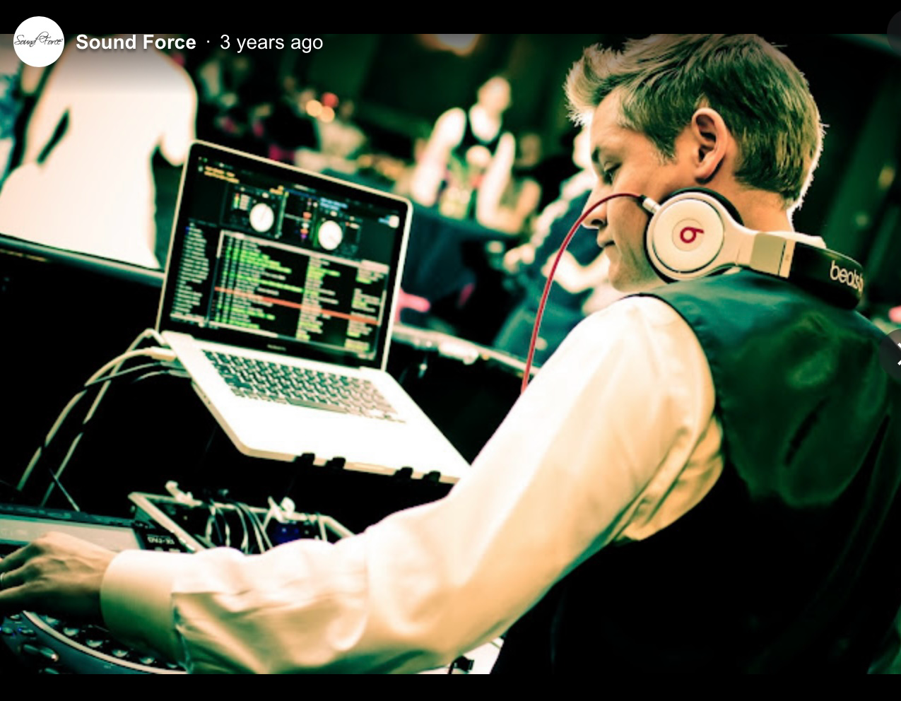 DJ wearing Beats headphones operates a laptop and synthesizer keyboard at a live music event.