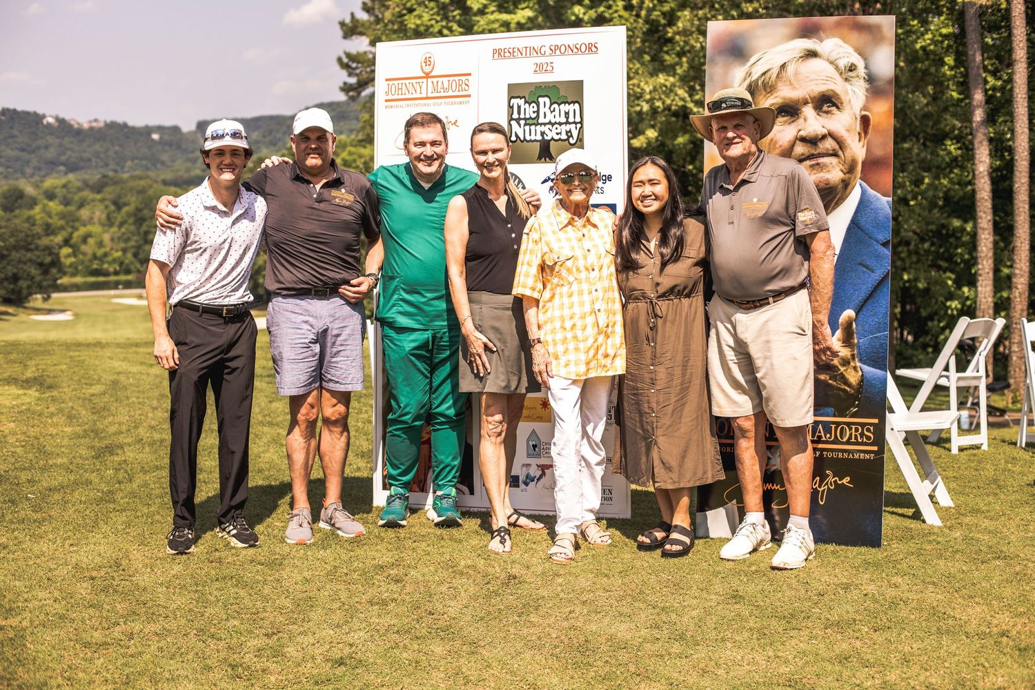 Group of seven people posing together outdoors at a golf charity event on a sunny day.