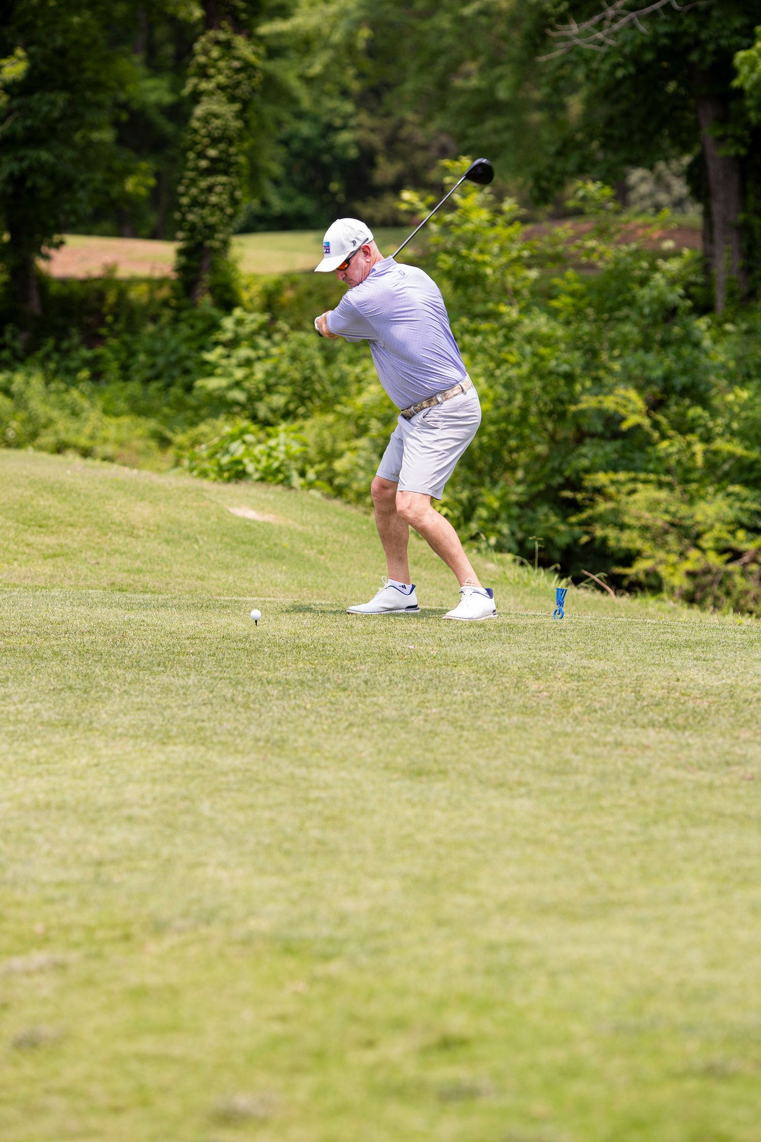 Golfer in white attire taking a swing on a lush green course.