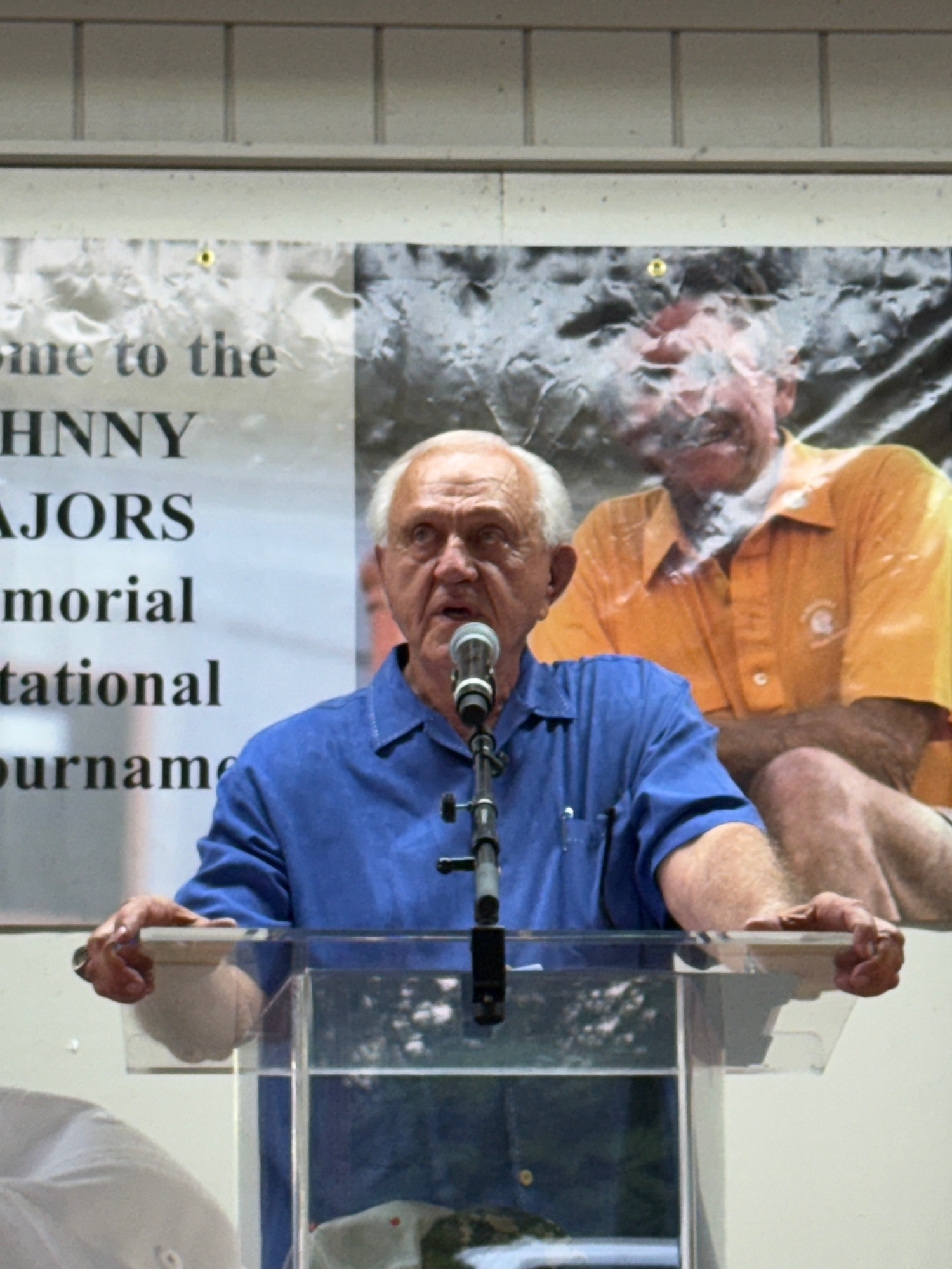 Man in blue shirt speaking at podium at Johnny Majors Memorial Invitational Tournament.