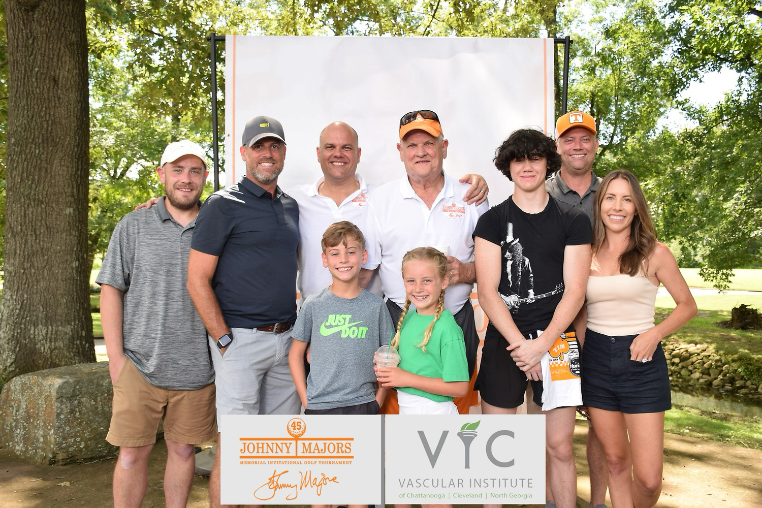 Group photo at VFC Vascular Institute golf event, adults and children posing outdoors near trees.