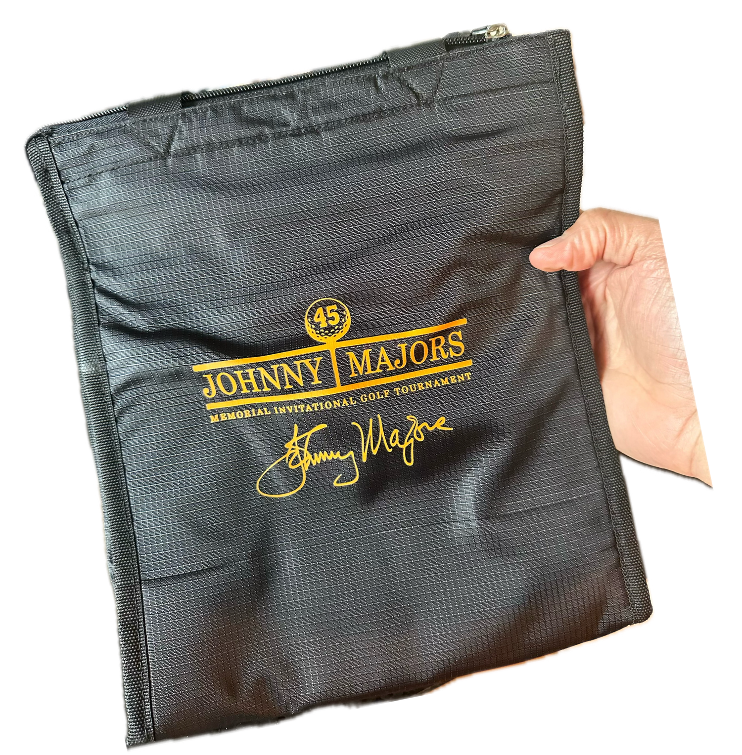 Black zippered bag with gold Johnny Majors Memorial Invitational Golf Tournament logo and signature, held by hand.