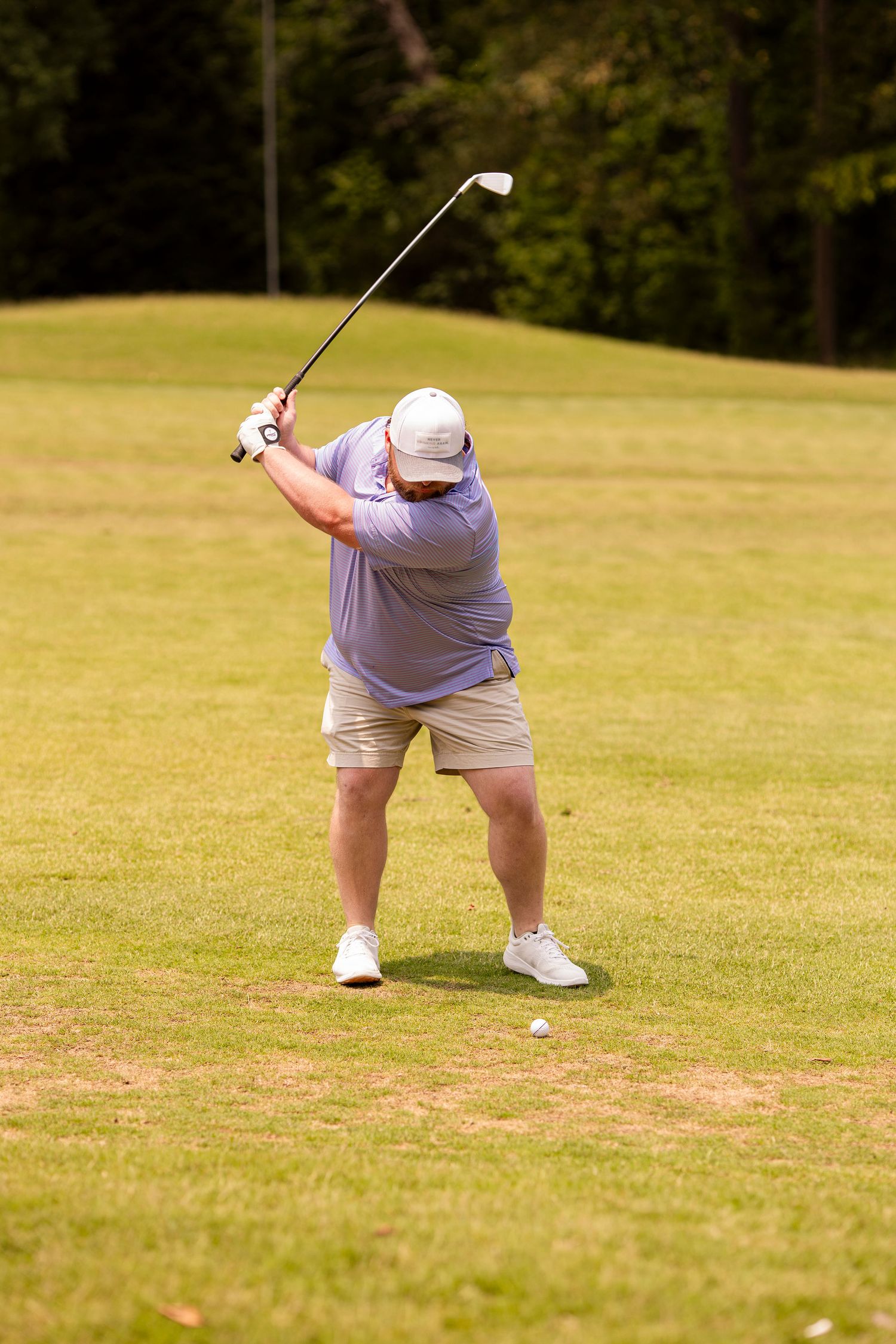 Golfer in purple shirt and khaki shorts taking a swing on the fairway.