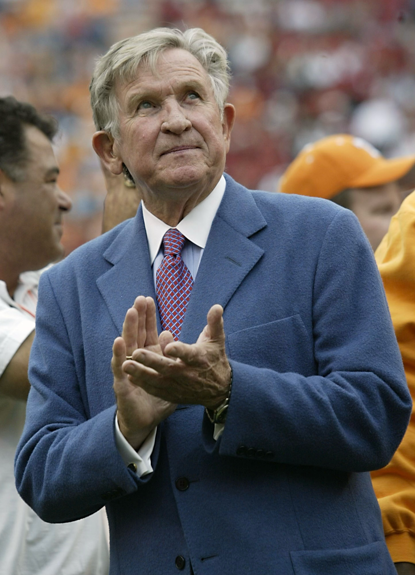 Man in blue suit and pink tie applauding enthusiastically at a sporting event.