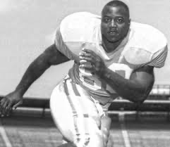 Vintage black and white photo of a football player in uniform carrying the ball during a game.
