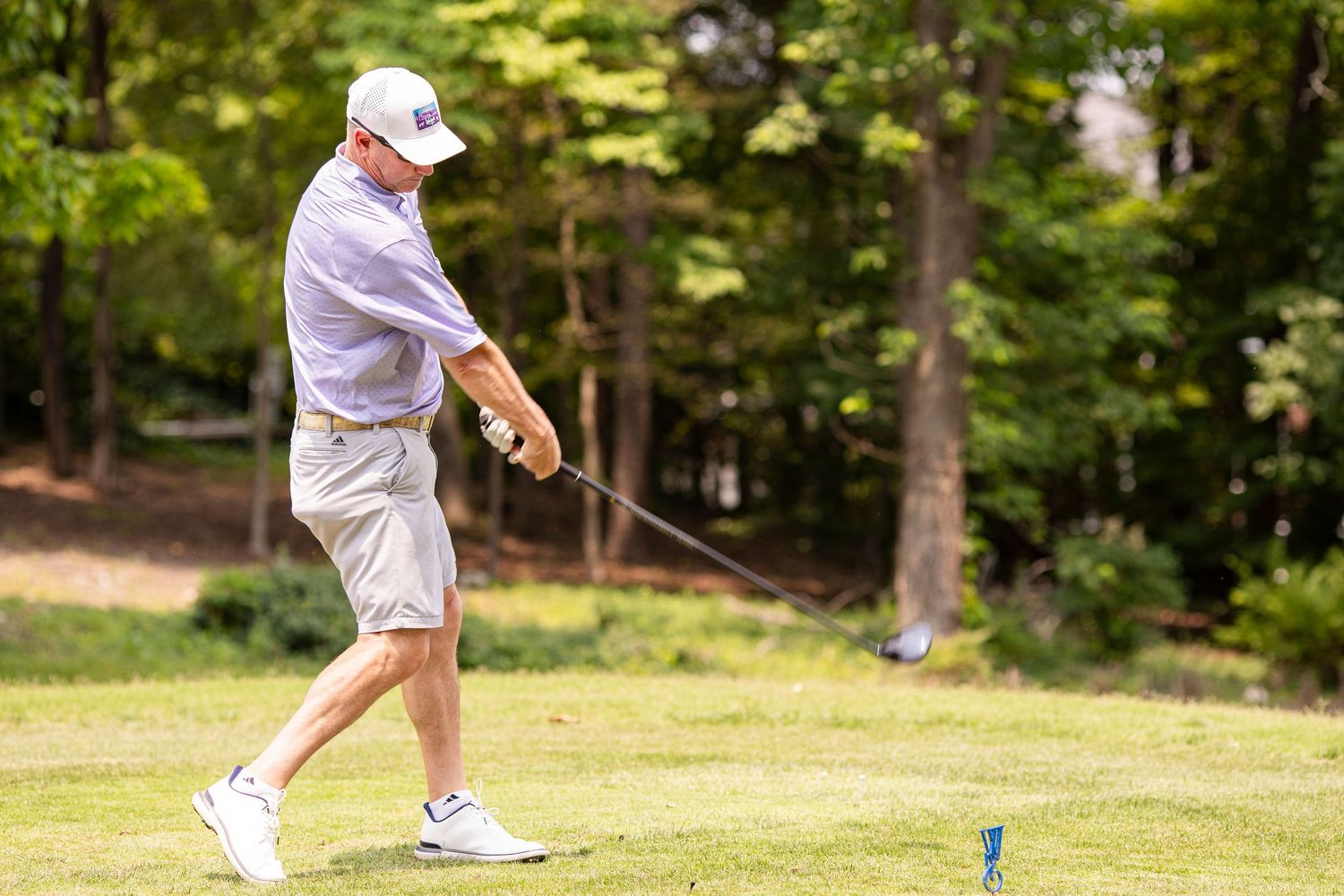 Golfer in white attire mid-swing on a sunny golf course.