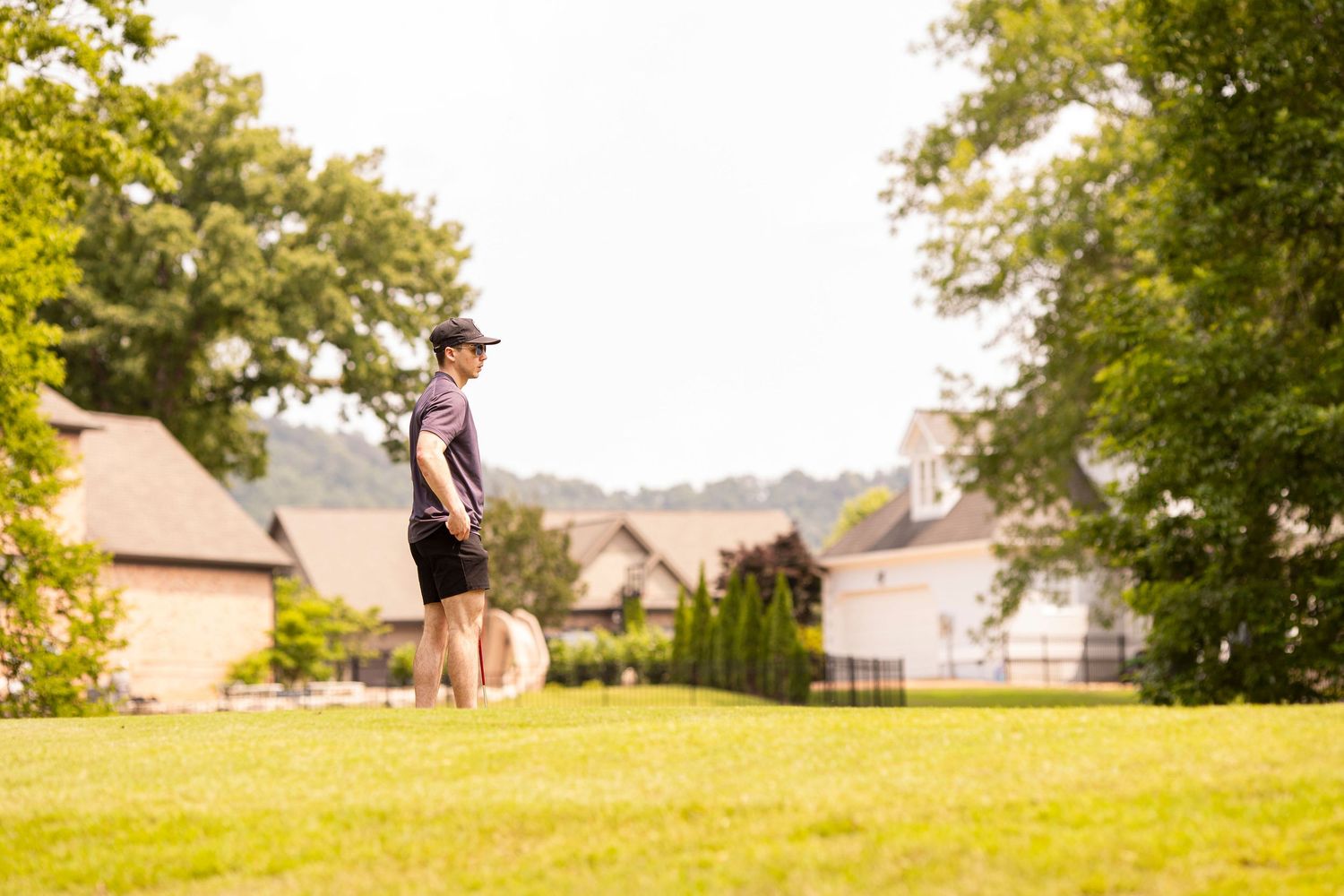 A person jumps high in the air on a sunny lawn with suburban houses in the background.