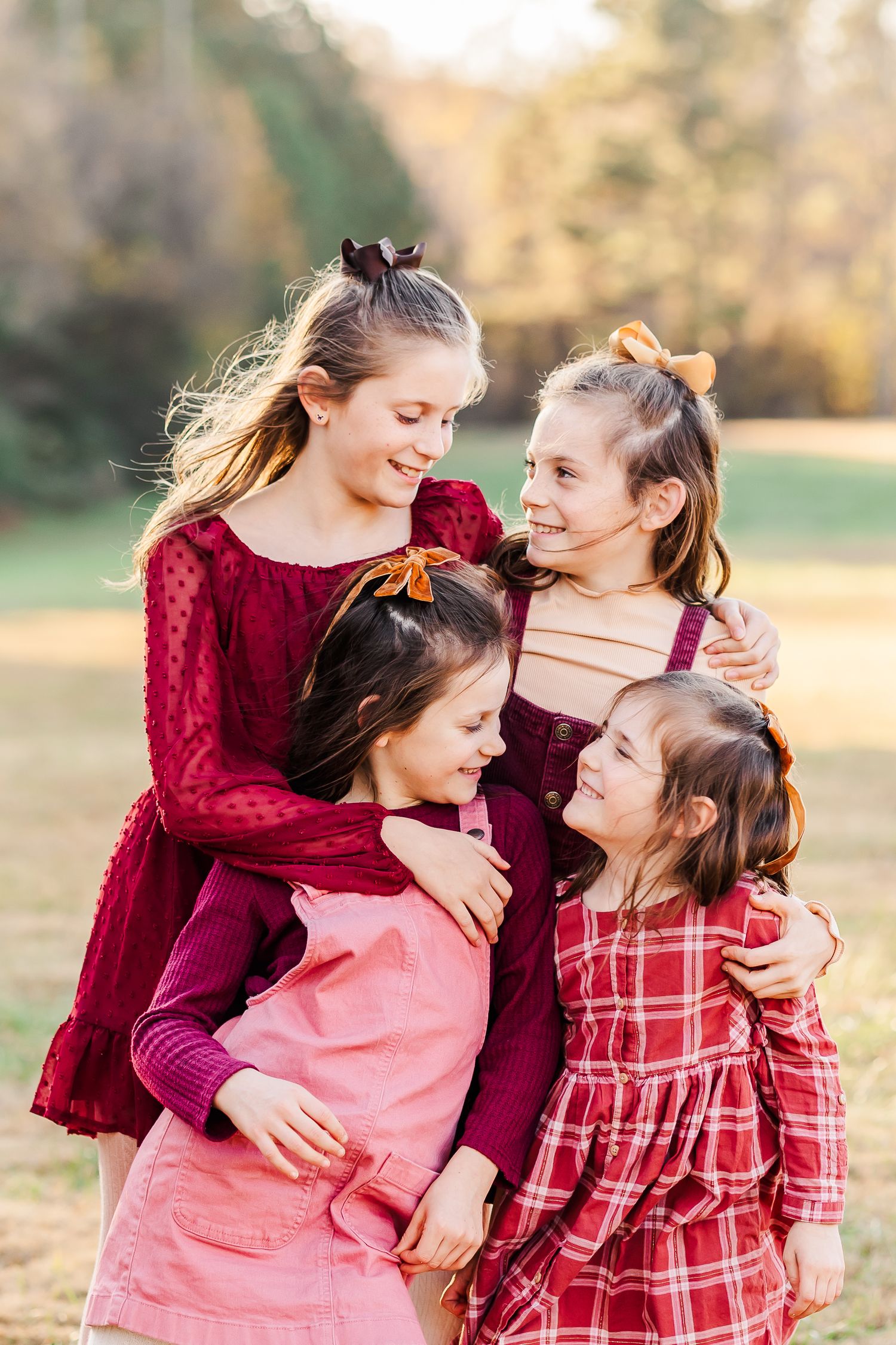 Four young sisters smiling and laughing at each other during family session at golden hour in Atlanta, Georgia.