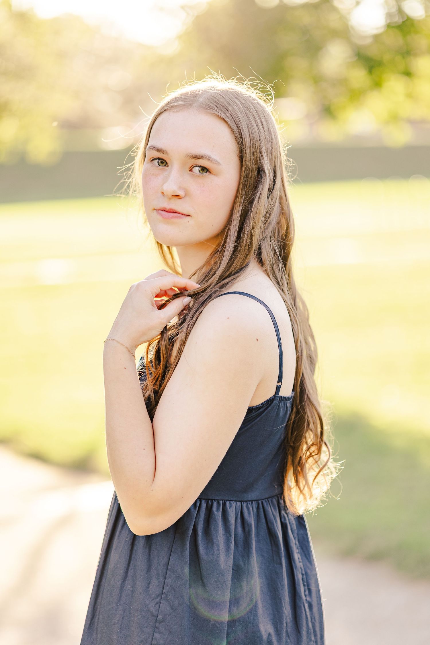 Young woman in navy dress posing outdoors in warm golden sunset light.