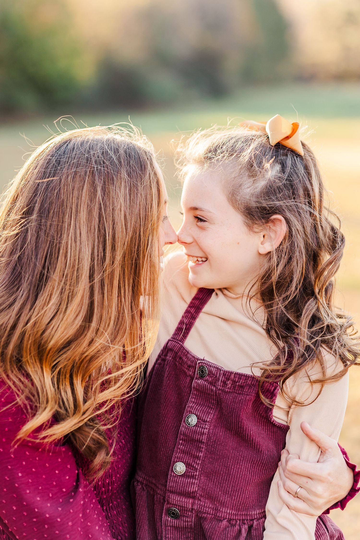 Mother and young daughter sharing a joyful nose-to-nose moment in warm outdoor natural light.