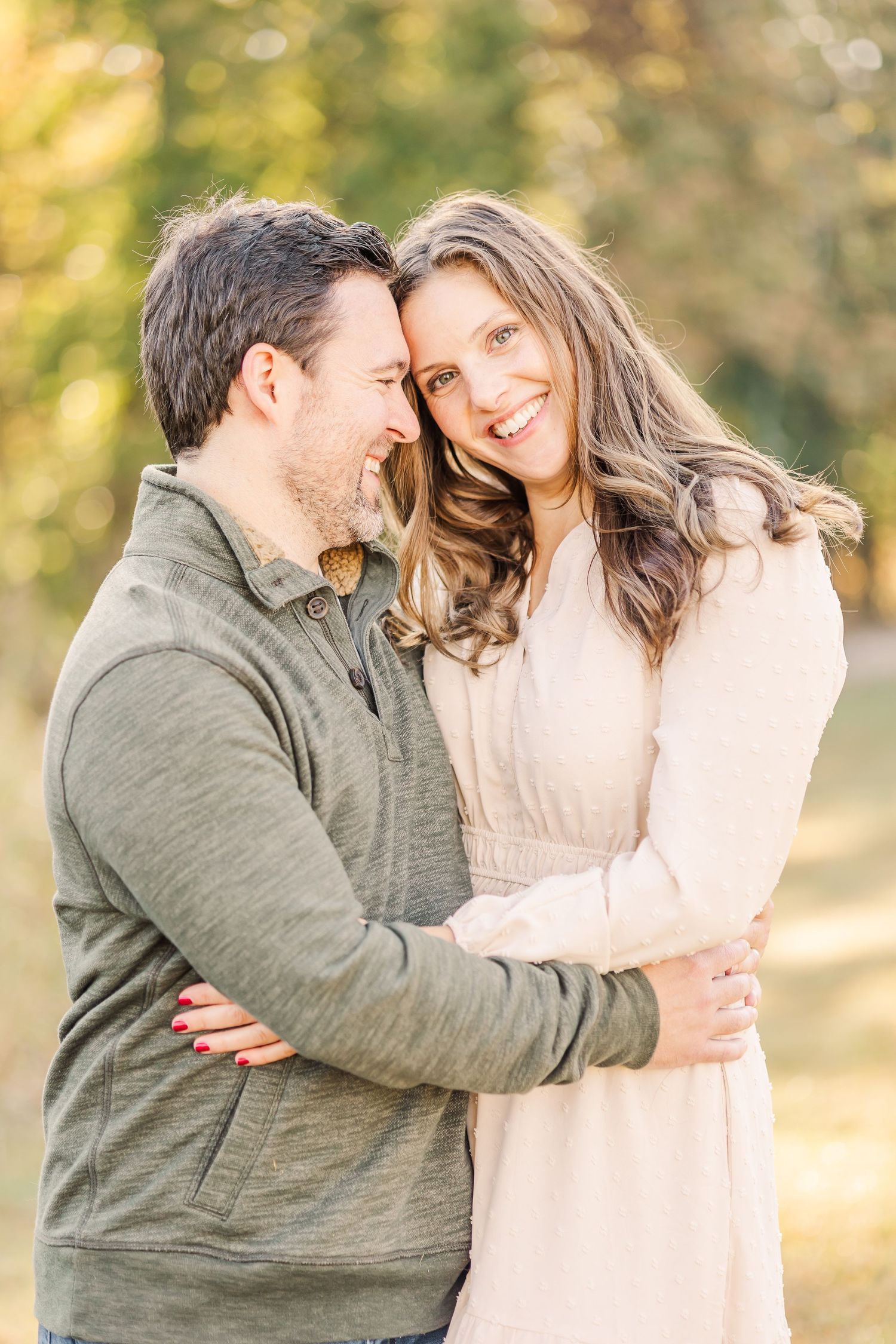 Couple embracing and smiling together outdoors during a warm golden hour family portrait session.