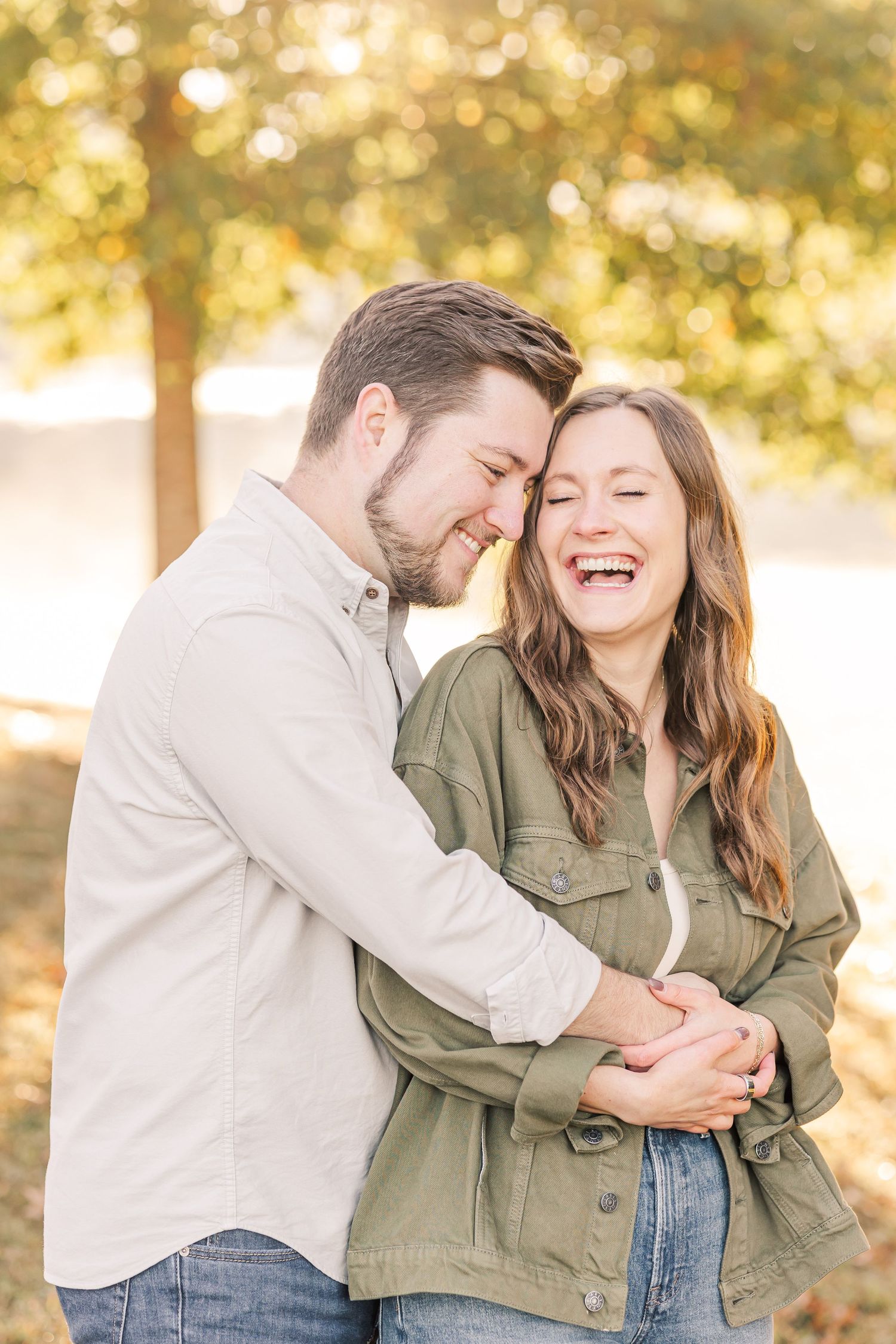 Laughing couple embracing outdoors with golden bokeh background in autumn park.