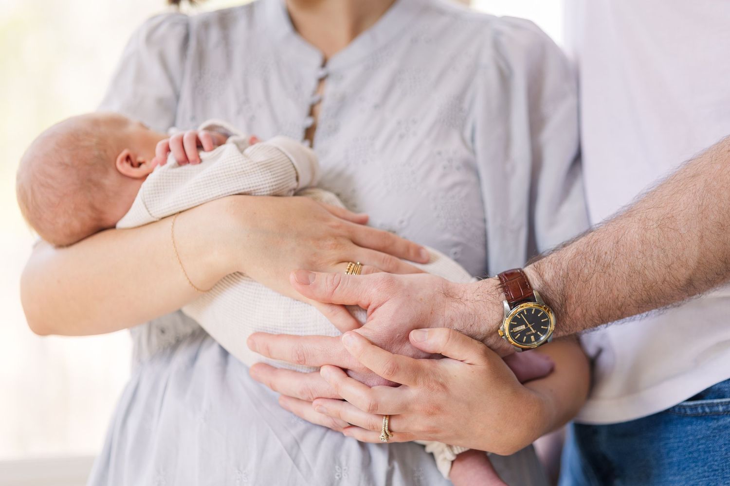 Parents cradling a newborn baby, with the father's hand gently supporting the infant in a tender family moment.