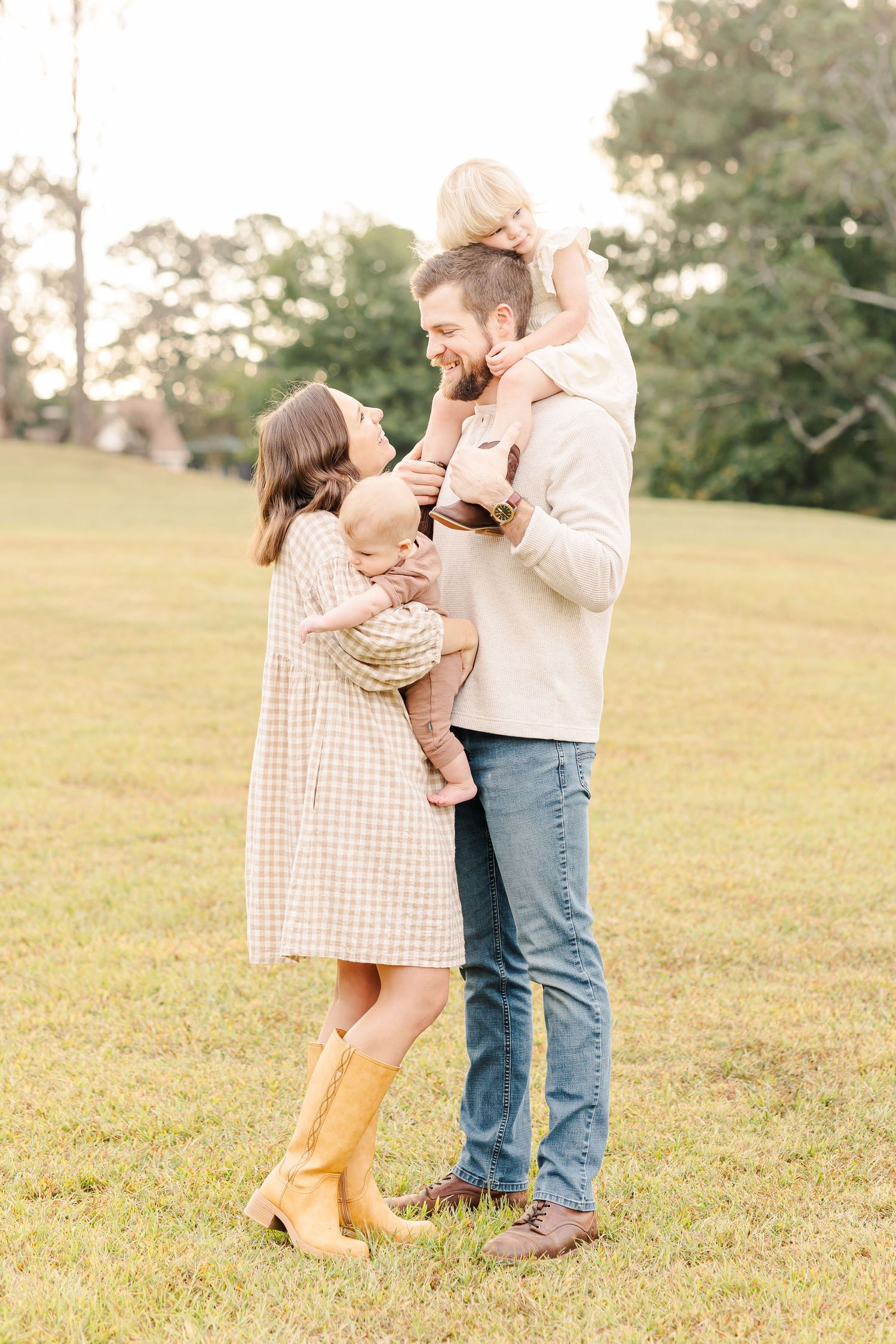 Happy family with two children standing together in sunny green field at golden hour.