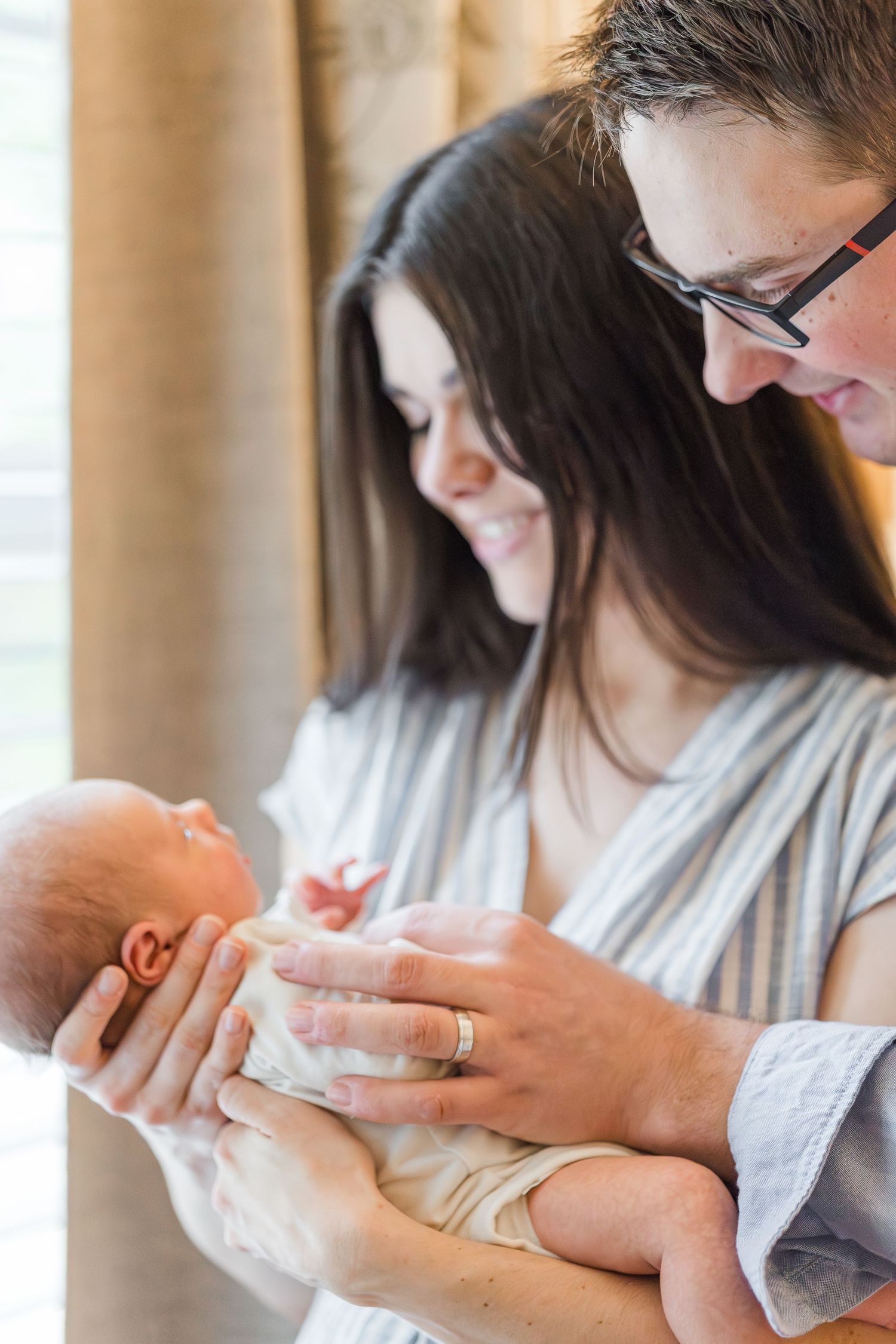 Happy parents smiling at their newborn baby, with father holding infant gently while mother looks on warmly.