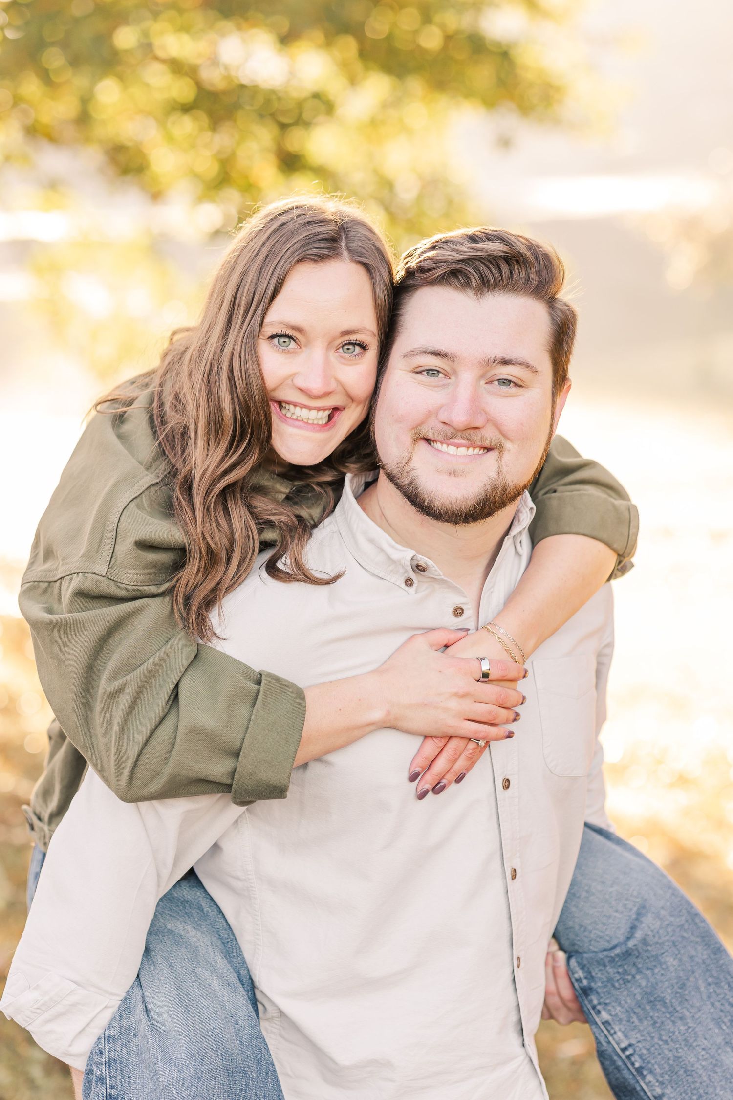 Smiling woman piggyback riding man outdoors with golden autumn bokeh background.