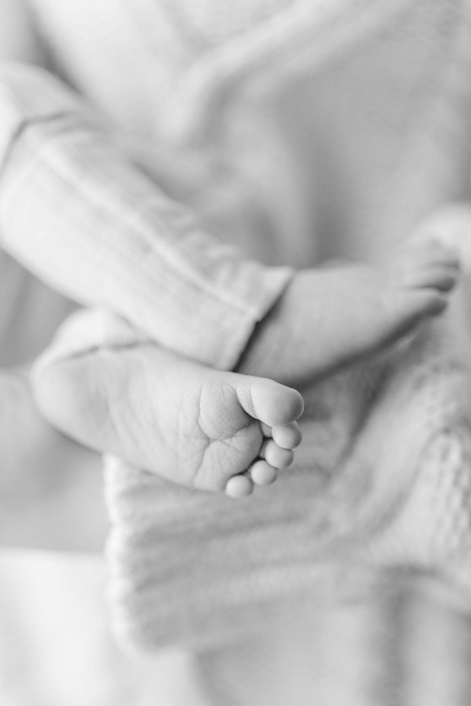 Black and white close-up of tiny newborn baby feet, delicate toes visible against mother's sweater.