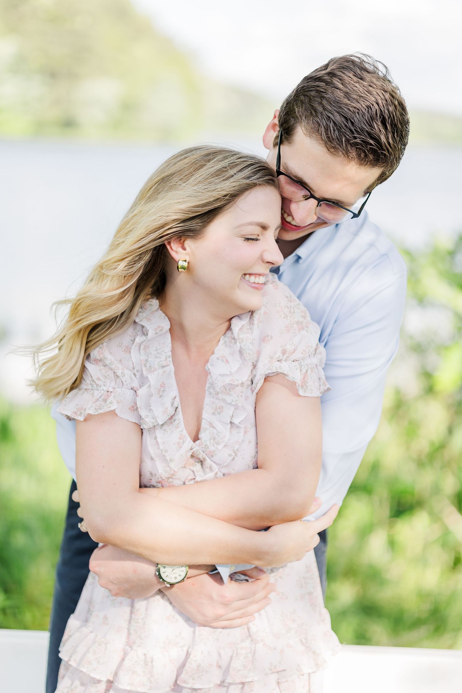 Happy couple embracing outdoors, man hugging smiling blonde woman near waterfront in soft natural light.