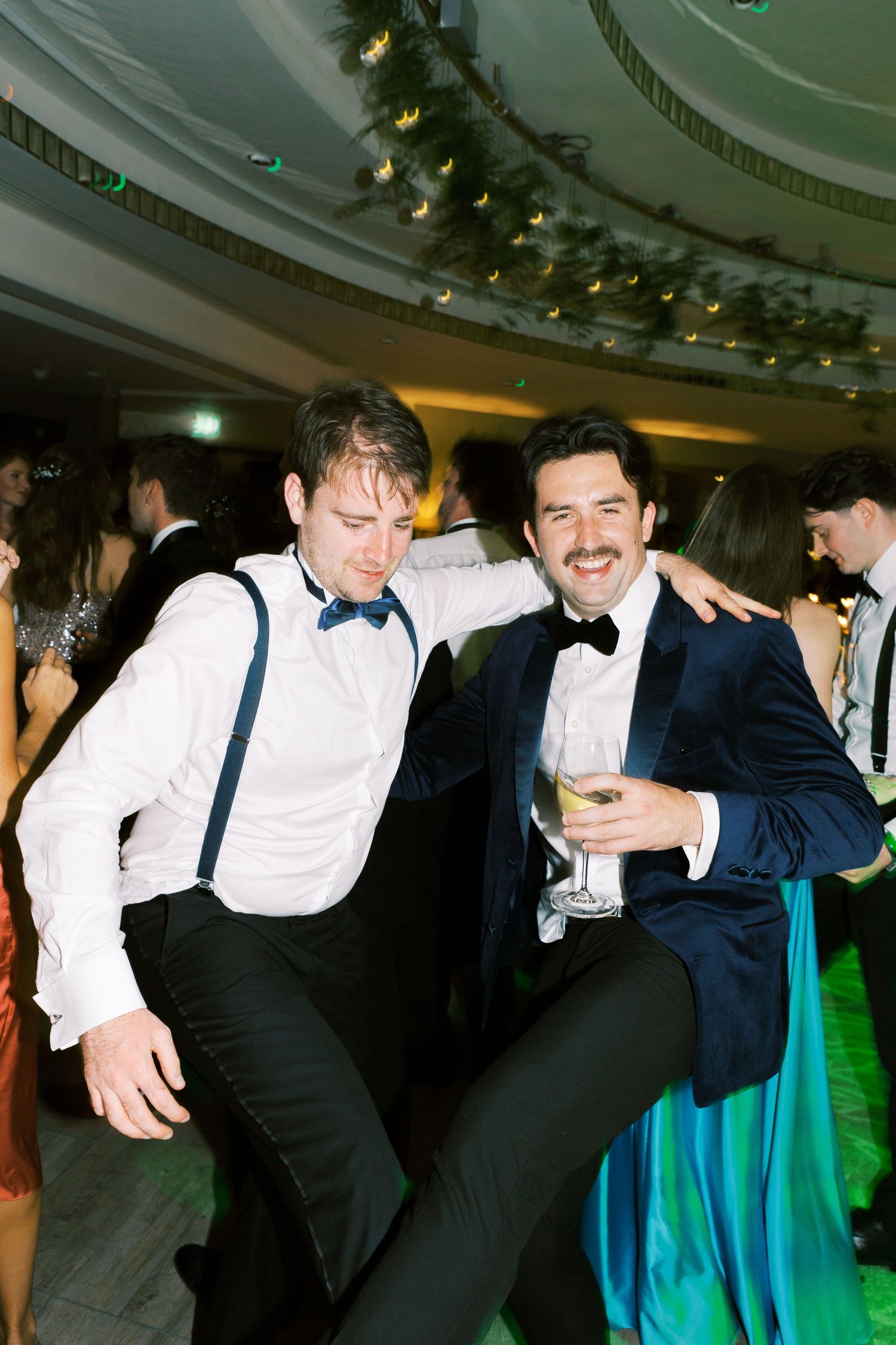 Two men in formal tuxedos dancing and celebrating together at an elegant wedding reception party.