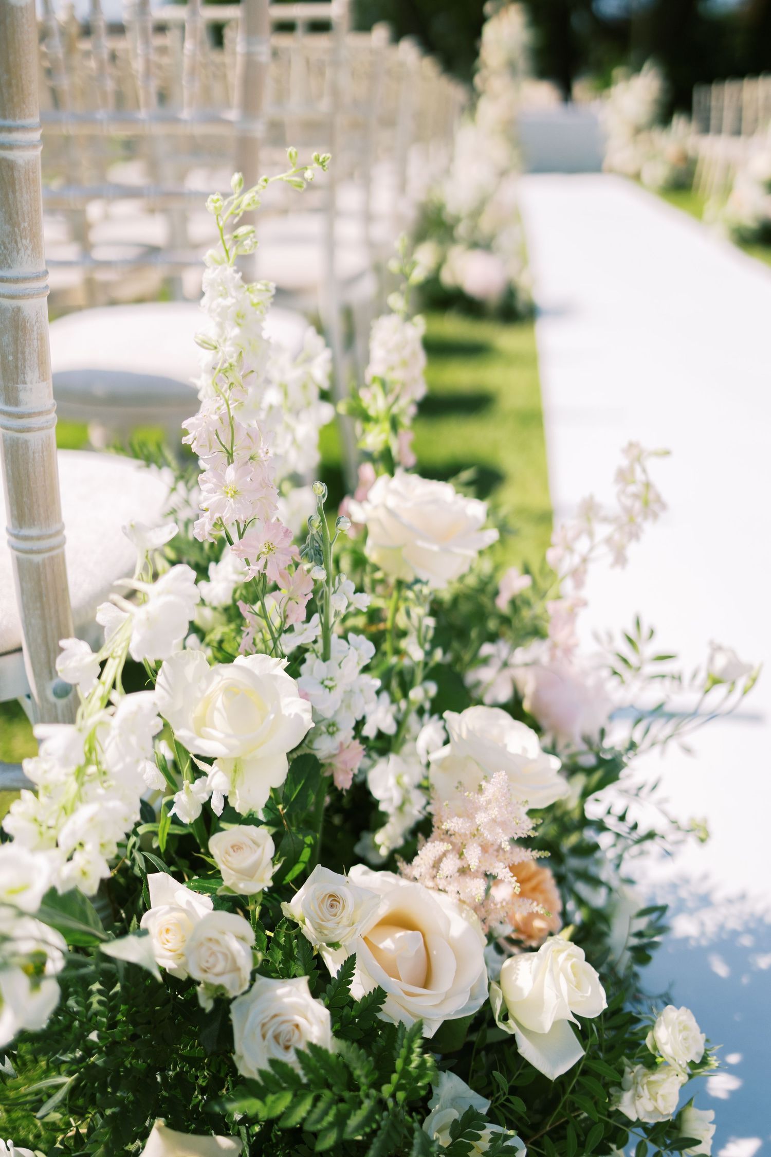 Elegant white rose floral arrangements lining outdoor wedding ceremony aisle.