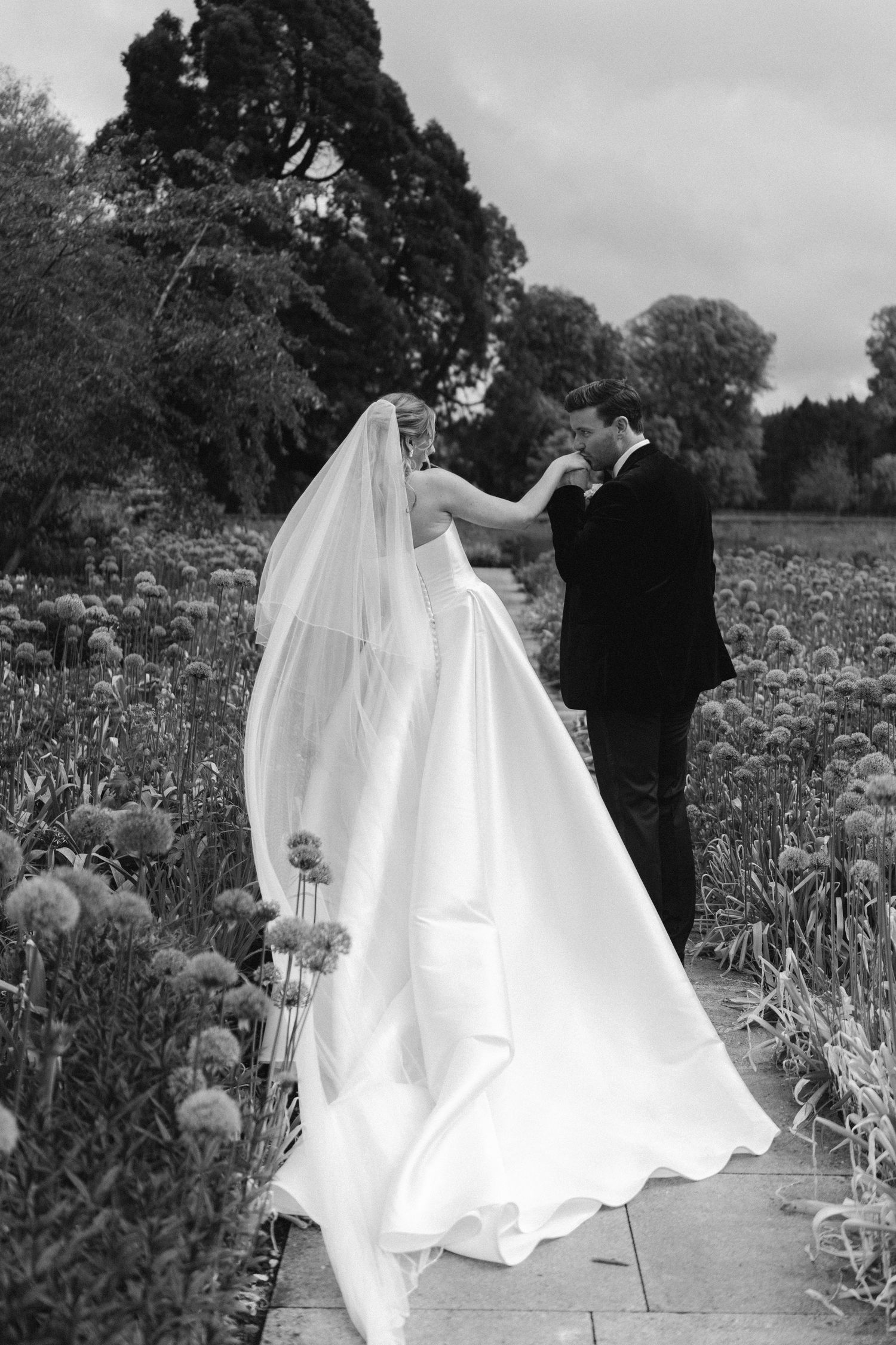 Black and white photo of a bride and groom sharing a romantic moment in a garden filled with allium flowers.