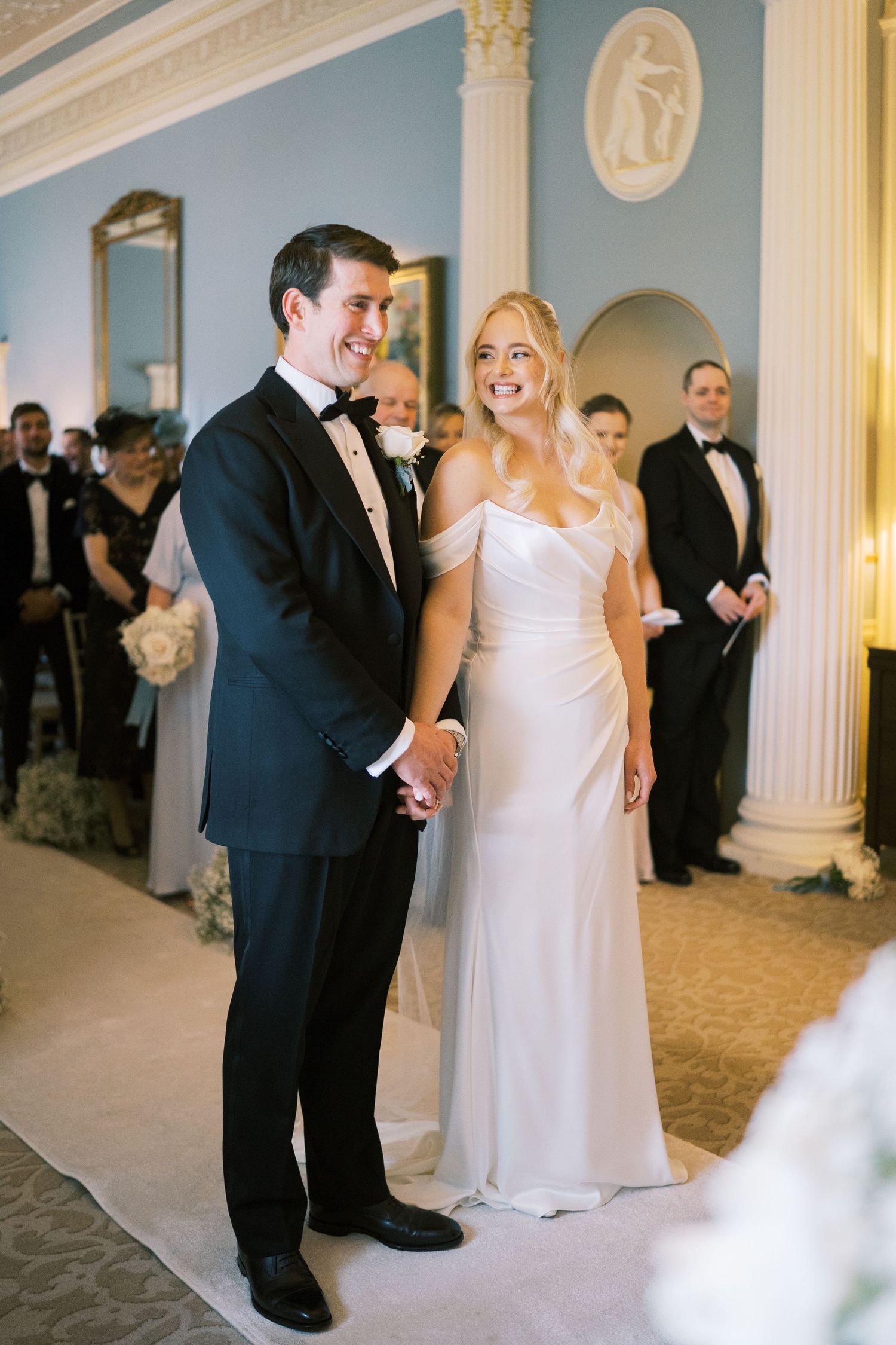 Bride and groom holding hands smiling during elegant indoor wedding ceremony.