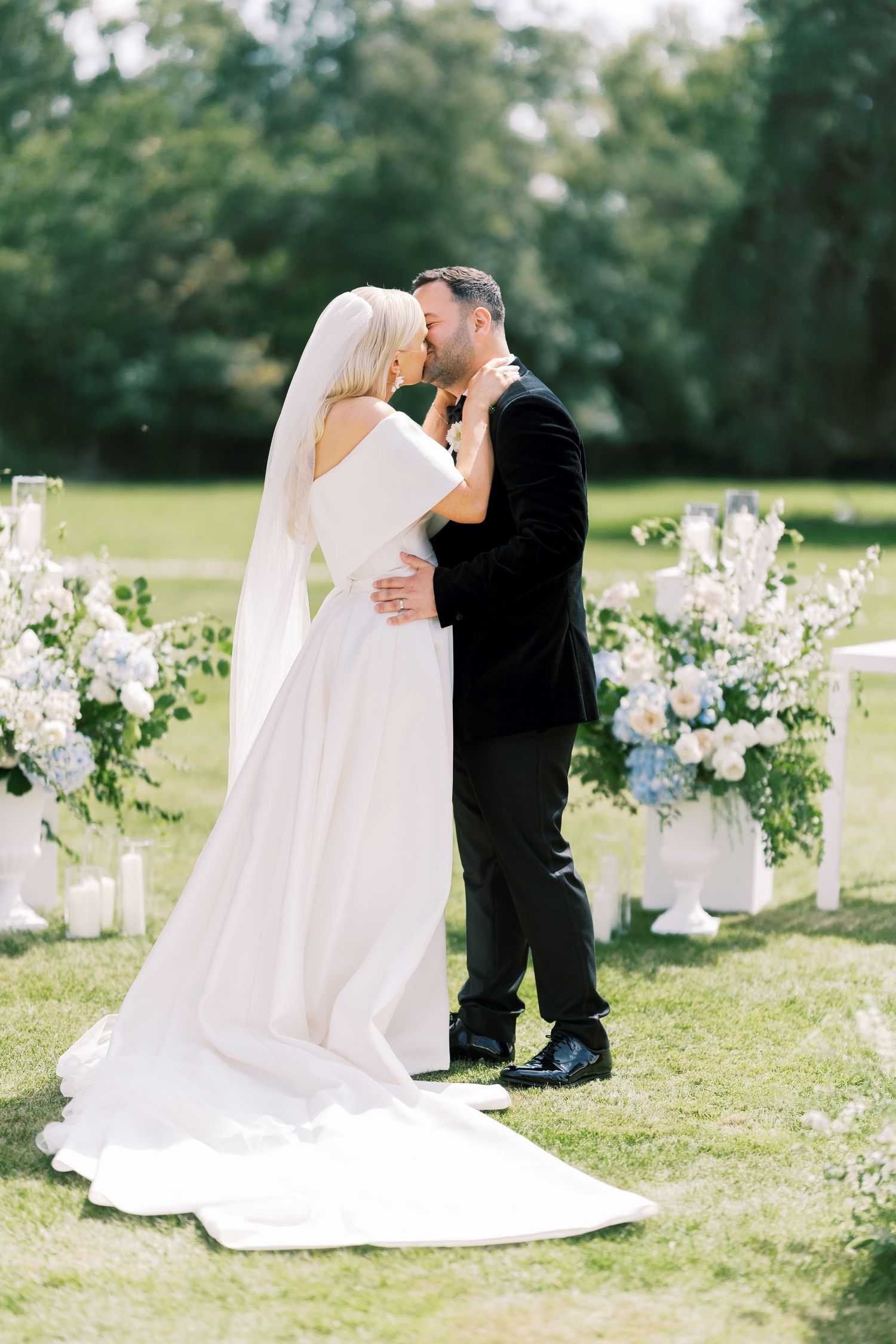 Bride and groom sharing first kiss at outdoor ceremony surrounded by blue and white florals.