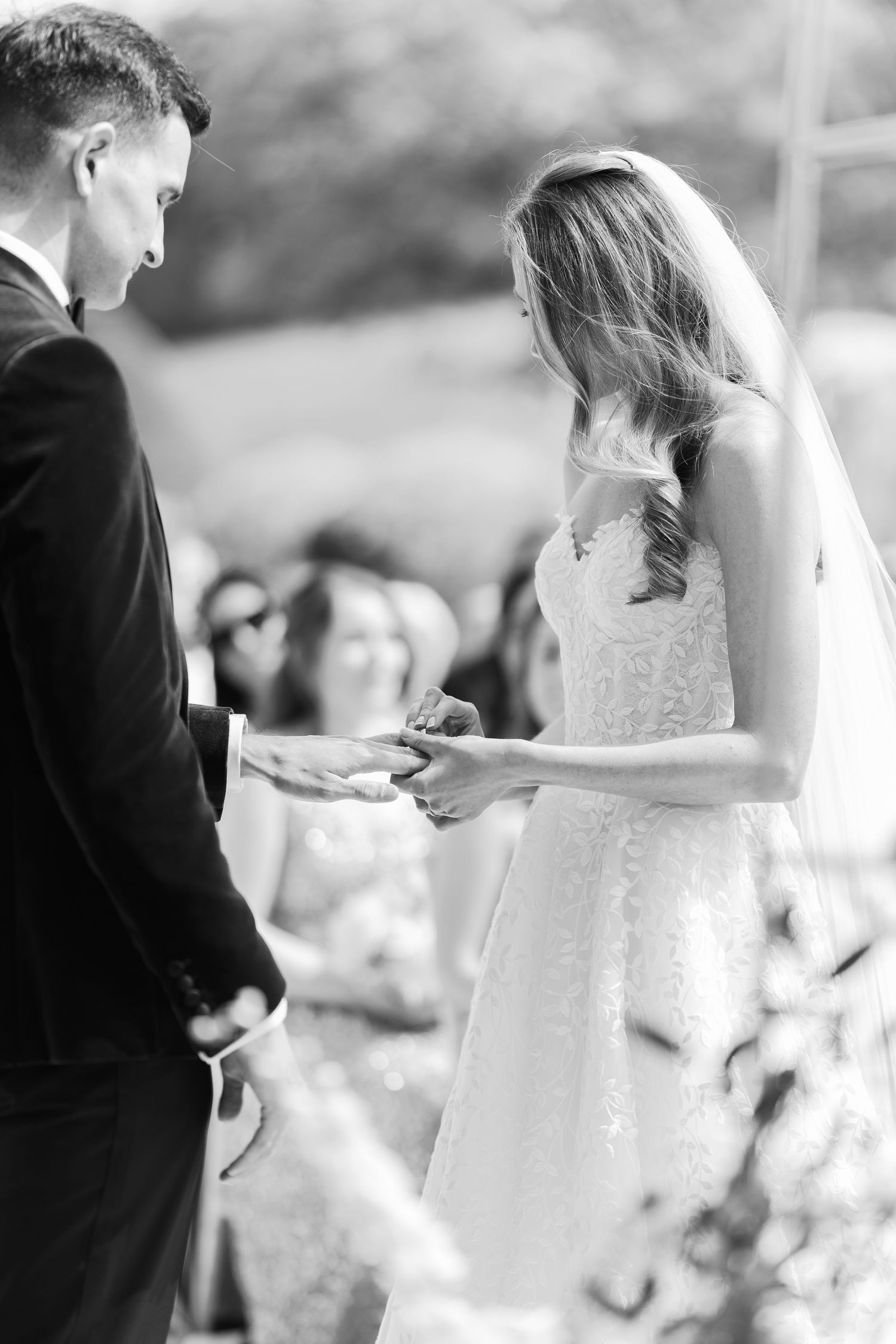 Bride and groom exchanging rings during outdoor wedding ceremony in black and white photo.