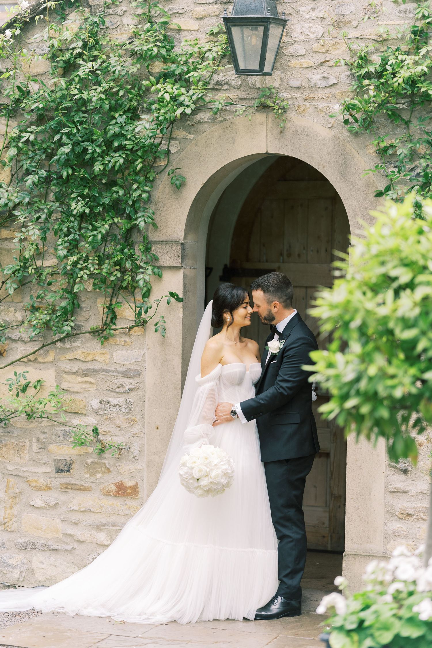 Bride and groom share a romantic moment in an arched stone doorway adorned with ivy, bride holding white bouquet.