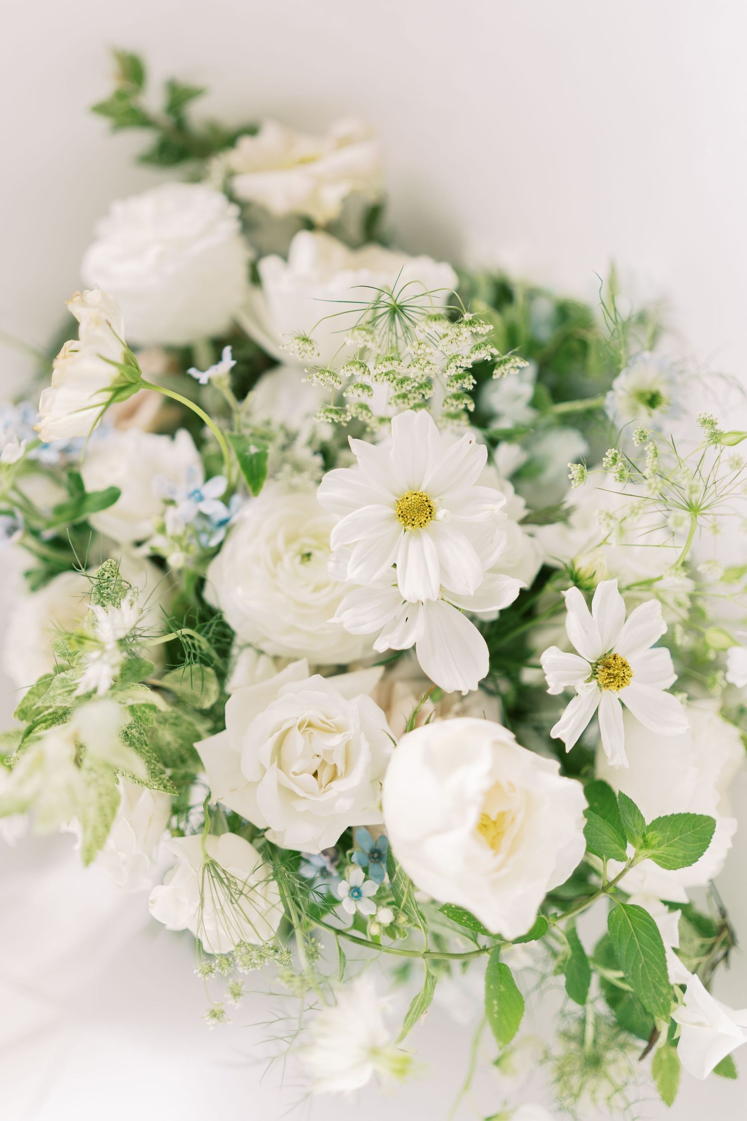 Lush white wedding bouquet featuring roses, cosmos, and delicate greenery with soft blue accents.