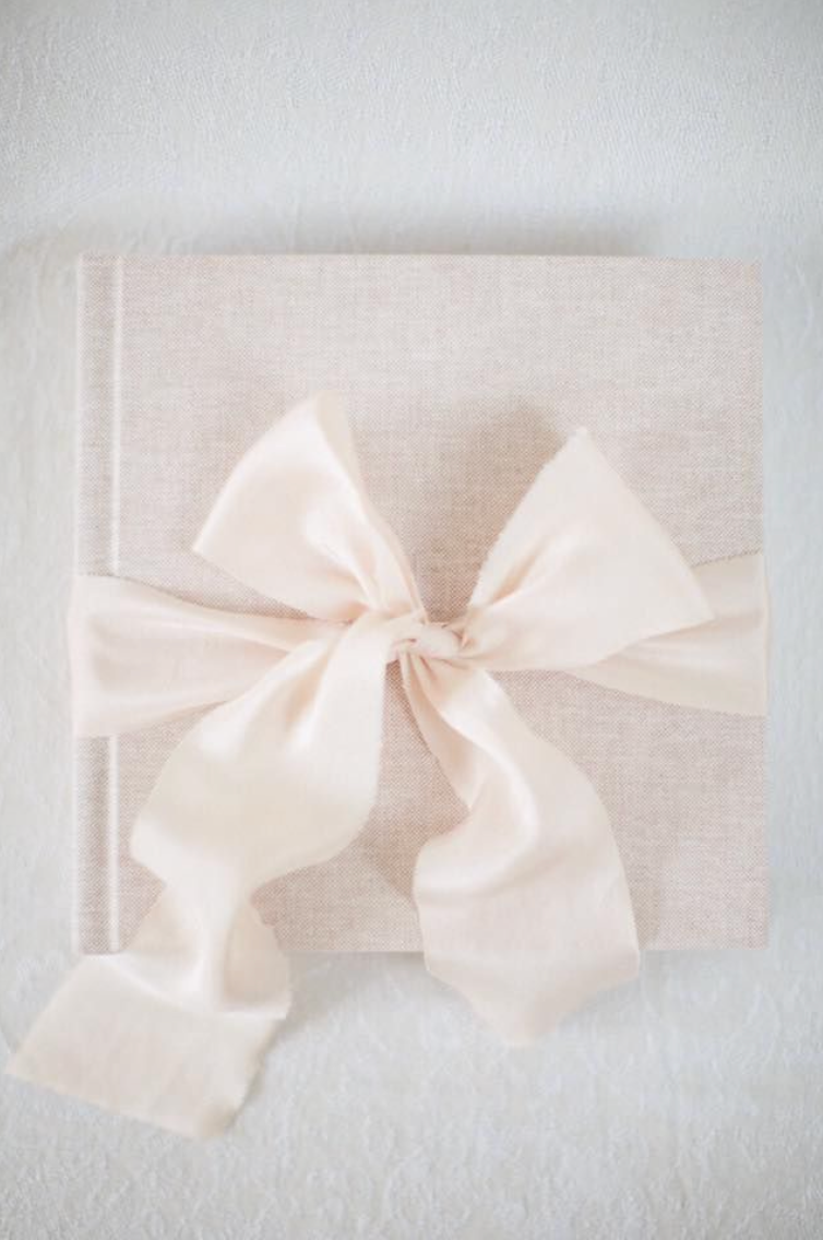 Elegant cream linen wedding guest book tied with a large satin ribbon bow on a white background.