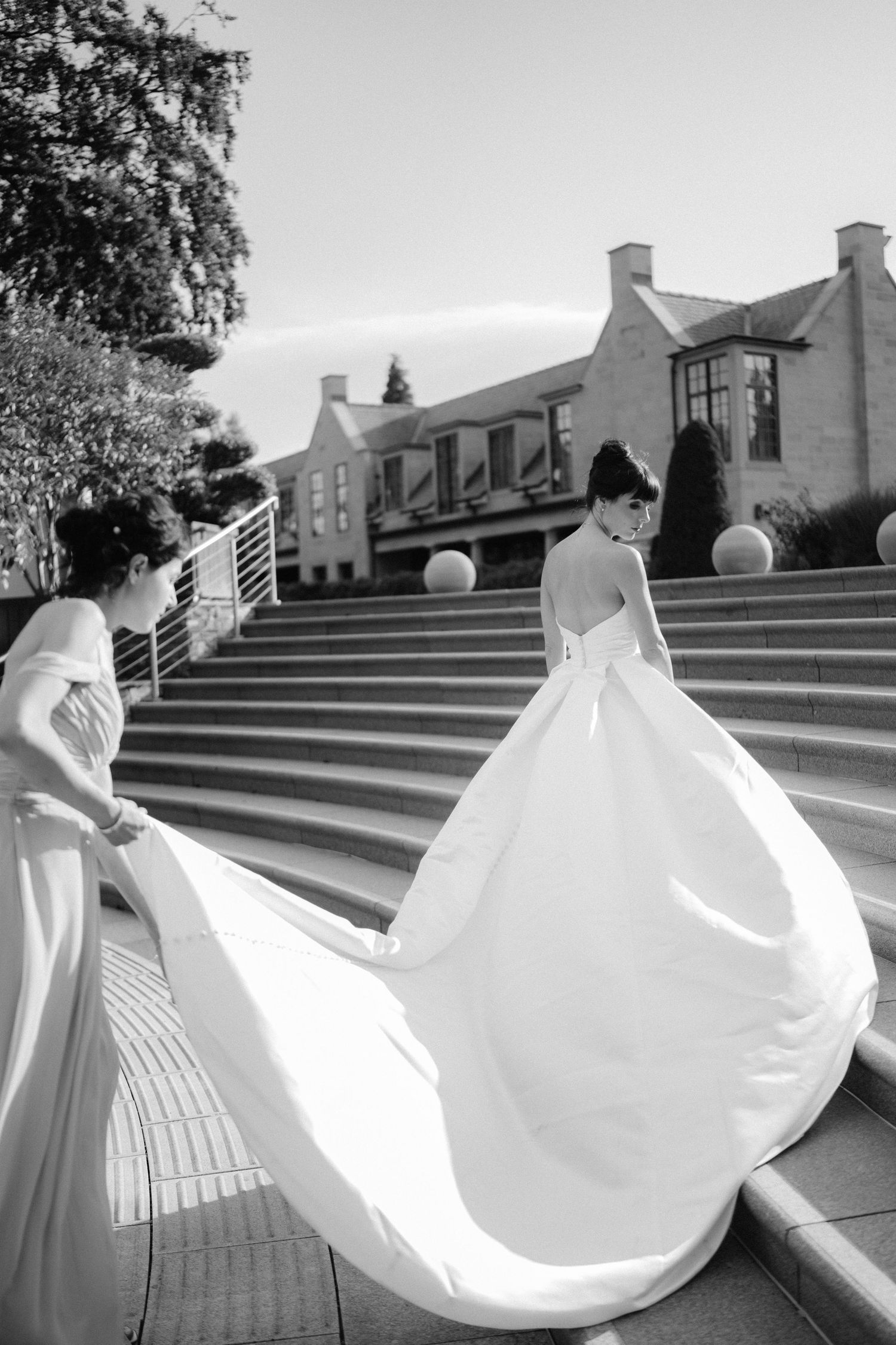 Black and white photo of a bride in a dramatic ballgown with long train ascending stone steps.