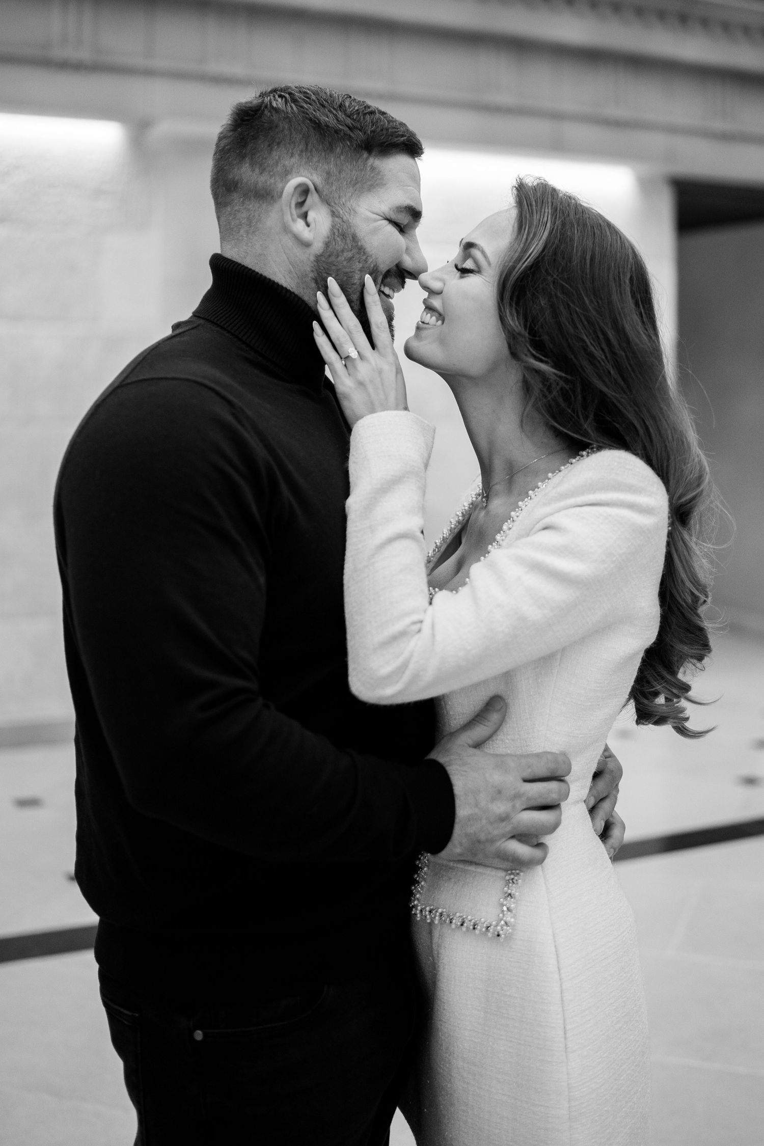 Black and white photo of happy engaged couple almost kissing, embracing in elegant venue.